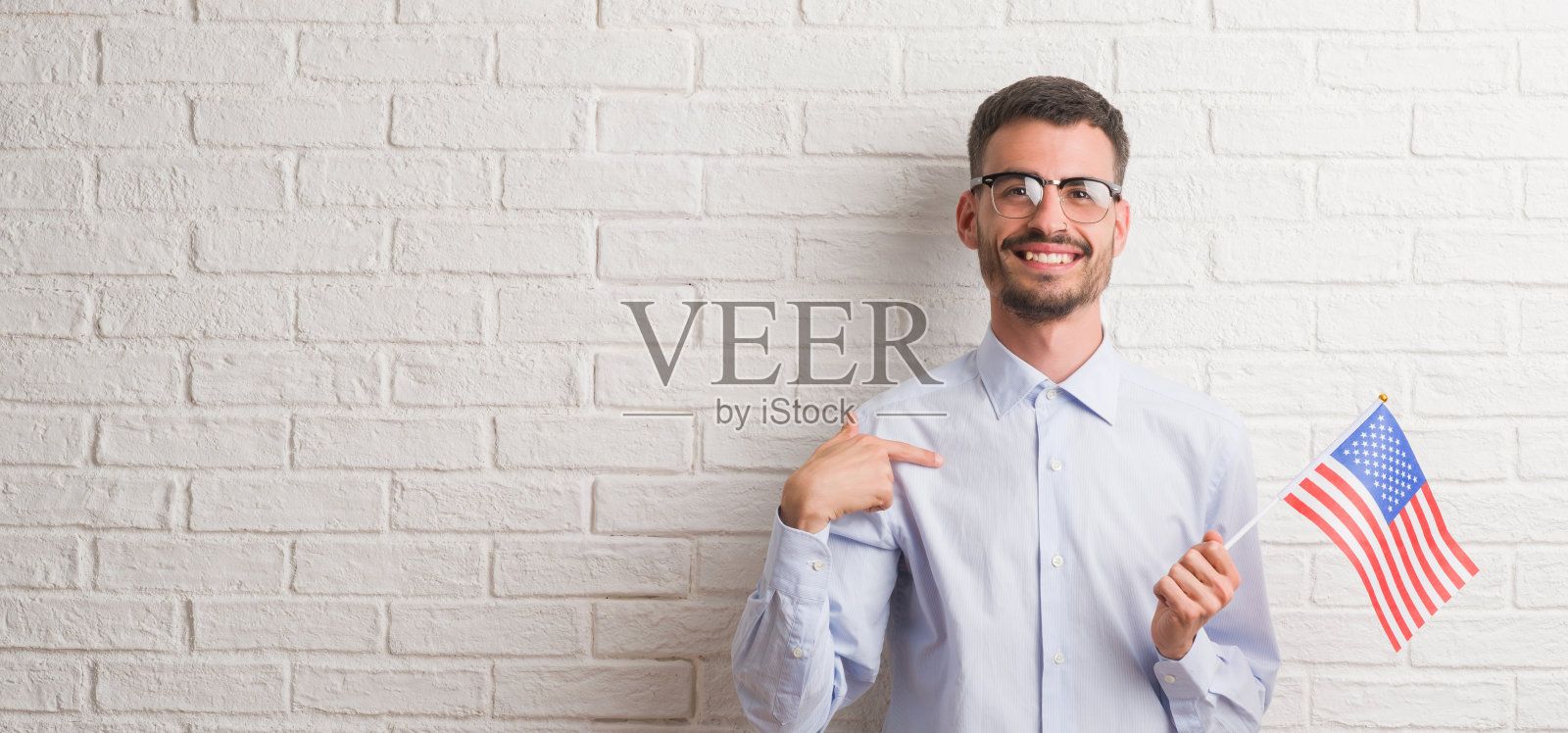 年轻的成年人举着美国国旗越过砖墙，惊讶地指着自己的脸照片摄影图片