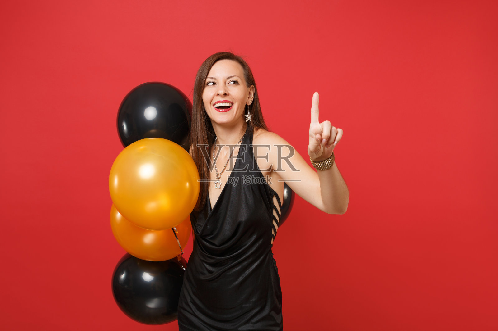 美丽的女孩庆祝拿着气球触摸像按钮指向浮动的虚拟屏幕孤立在红色背景。新年生日模型节日派对概念。照片摄影图片