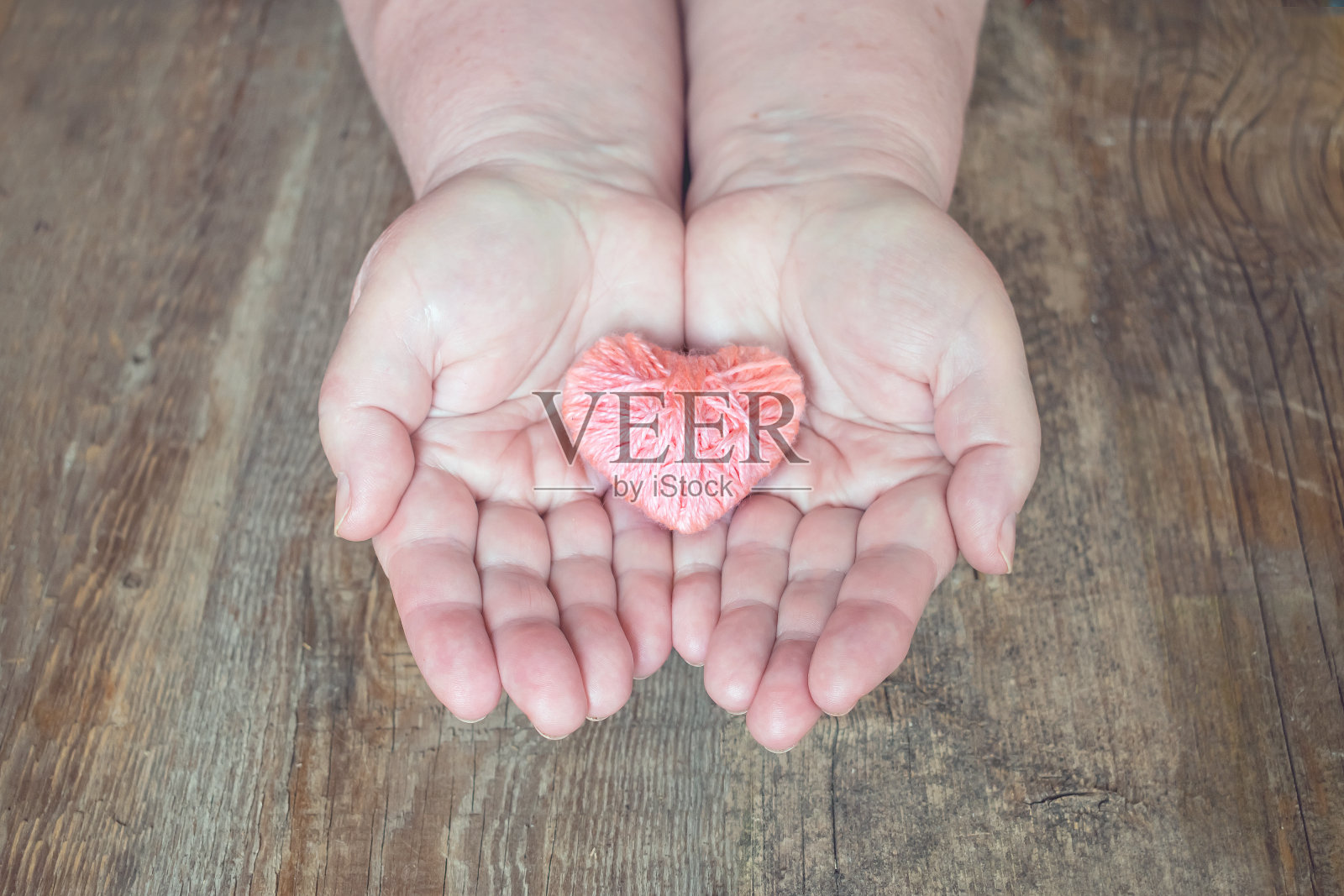 器官捐赠，帮助他人。成年女子双手给线红心。成年女子的双手，母亲在黑木背景上捧着一颗红心照片摄影图片