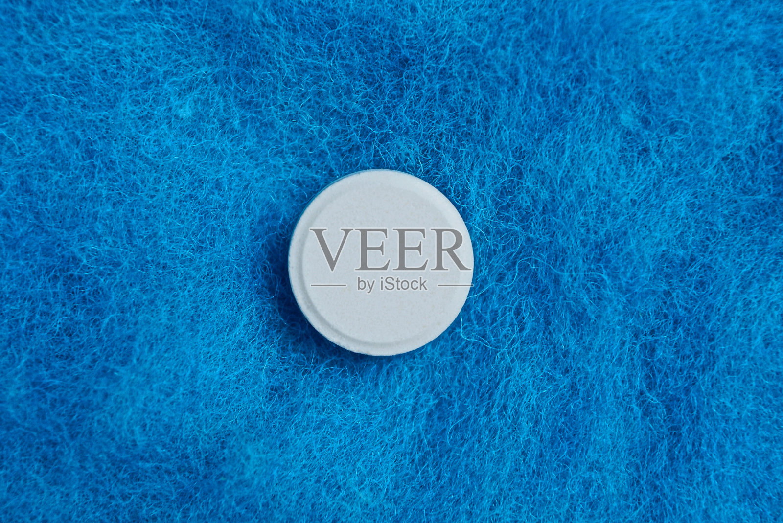 蓝色羊毛背景上的一个圆形的白色药片照片摄影图片