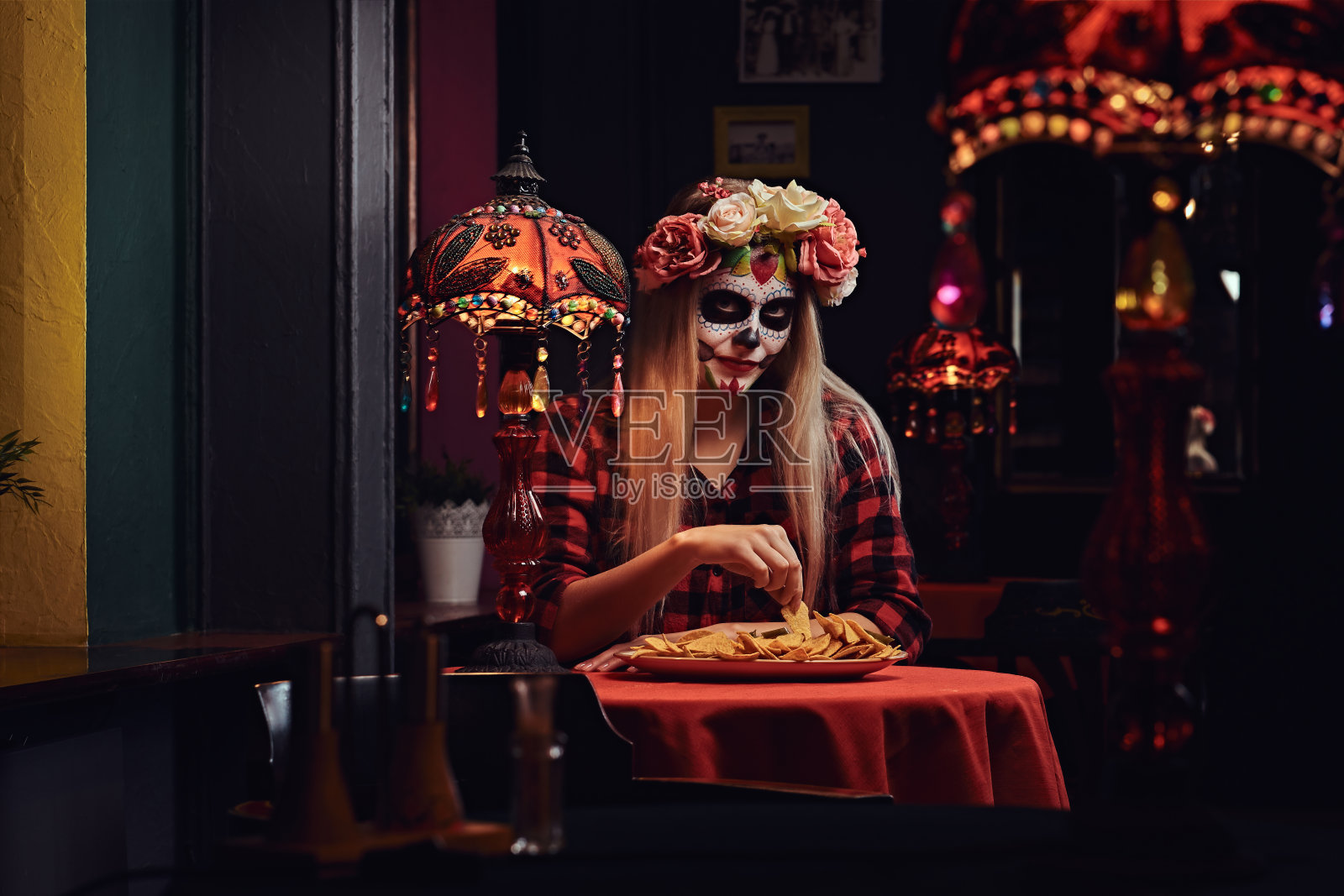年轻金发女孩在墨西哥餐厅化着僵尸妆，戴着花环吃玉米片照片摄影图片