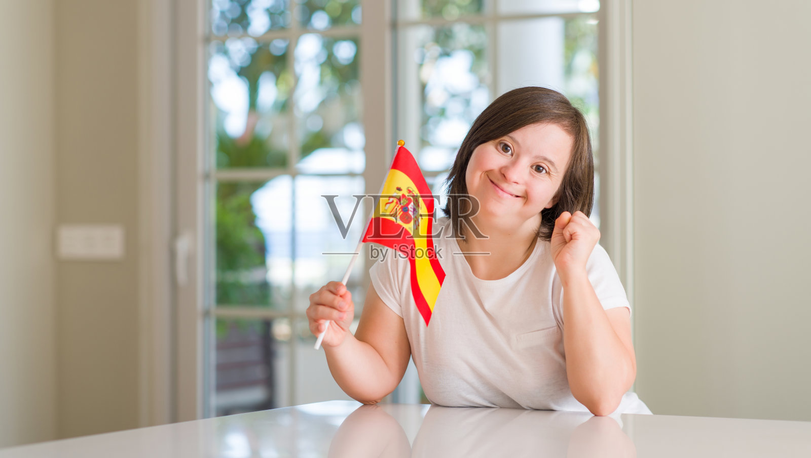 在家手持西班牙国旗，为胜利和成功欢呼雀跃的唐氏综合征女性，非常激动照片摄影图片