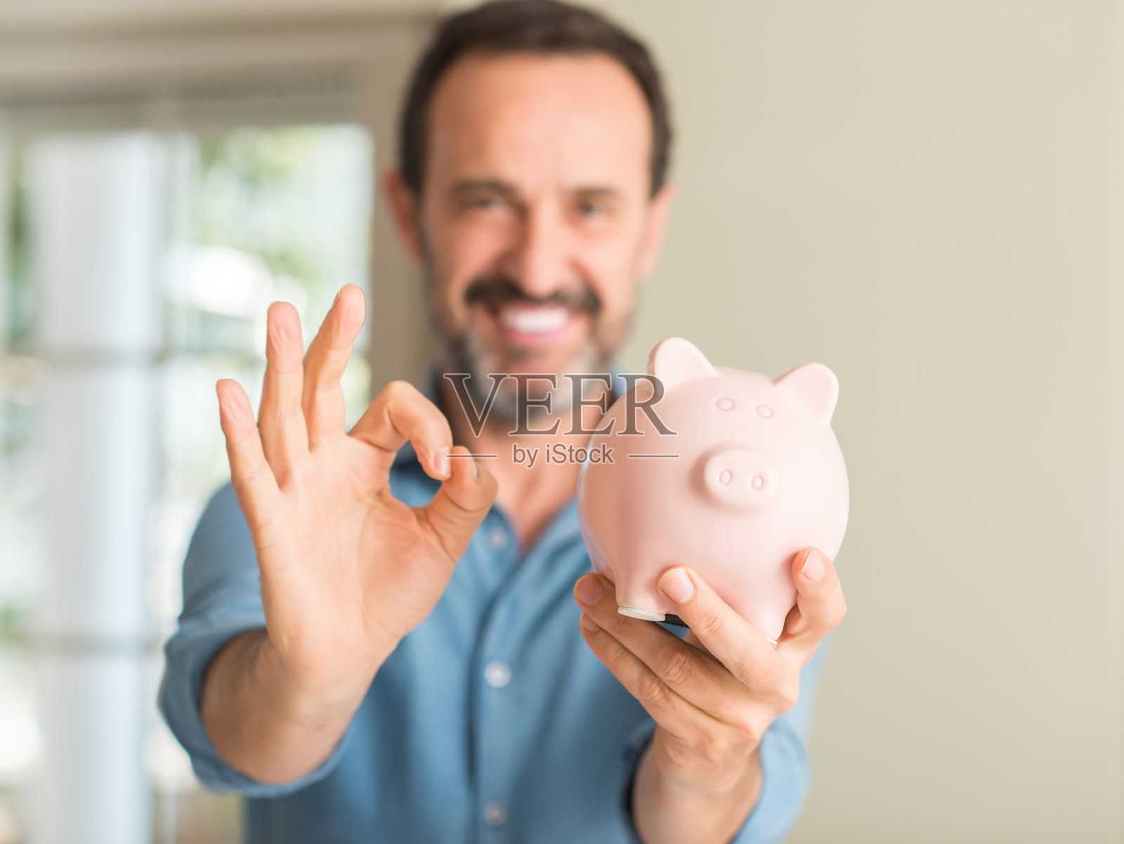 中年男人在存钱罐里存钱用手指做ok手势，很好的象征照片摄影图片