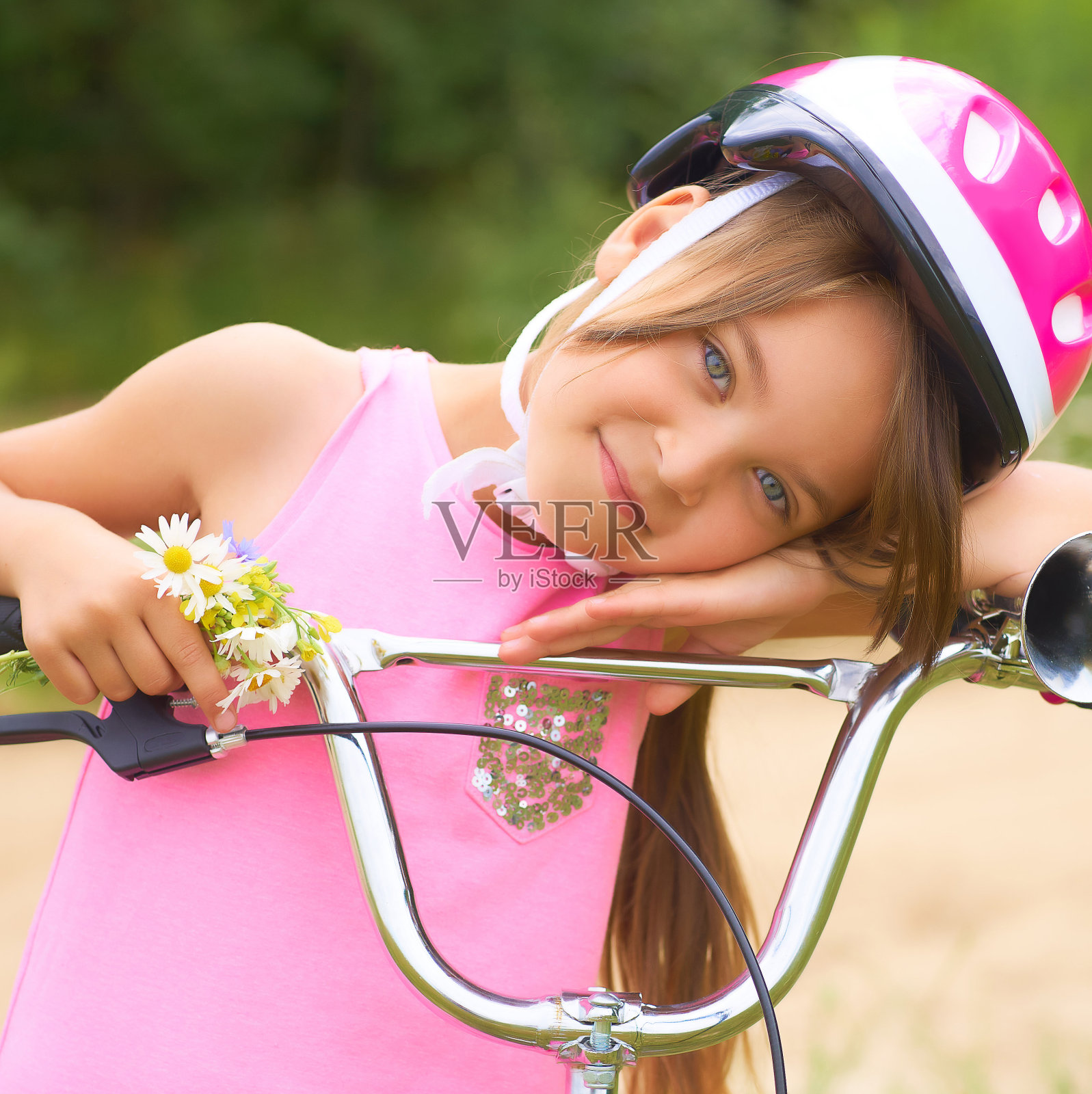 一个小女孩的肖像在一个保护头盔控制她的自行车和持有一束雏菊。照片摄影图片