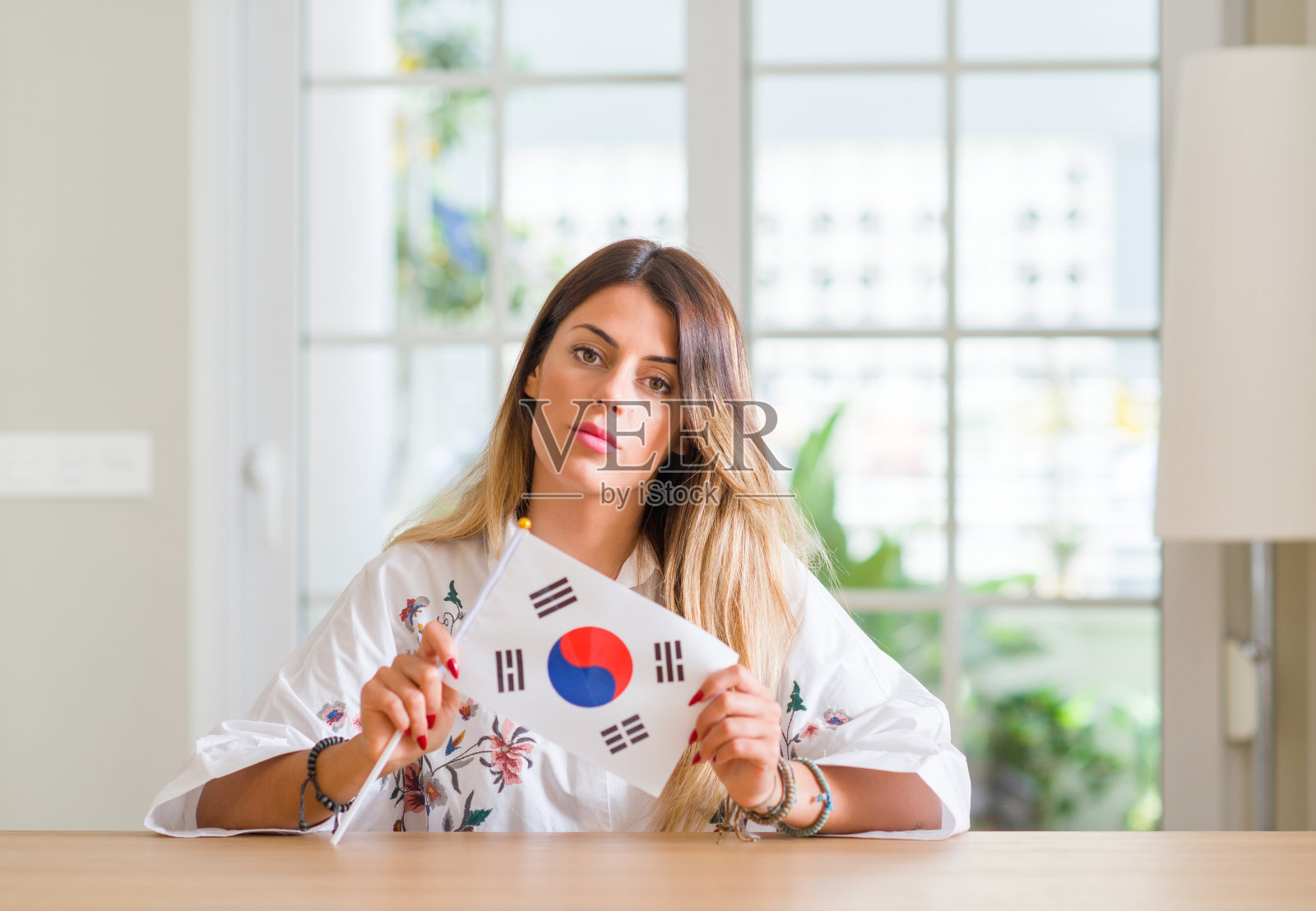 年轻女子在家中举着韩国国旗，聪明的脸上带着自信的表情认真思考照片摄影图片
