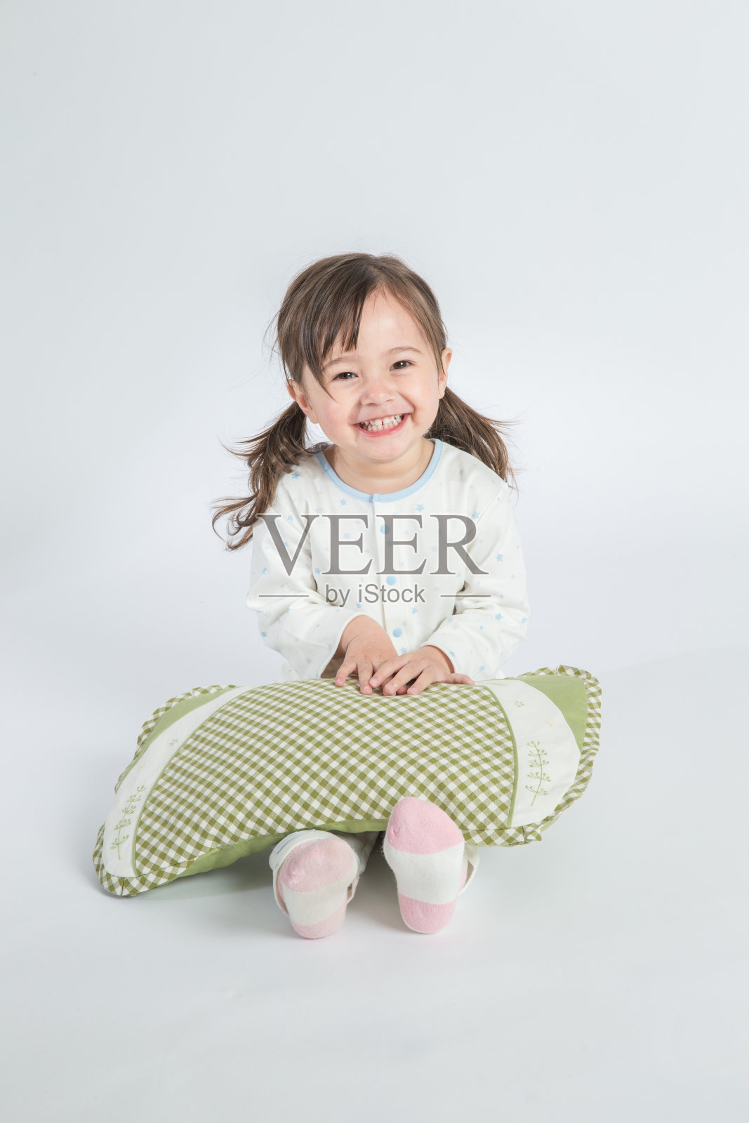 在白色的背景中，一个漂亮的小女孩拿着枕头坐在地板上照片摄影图片