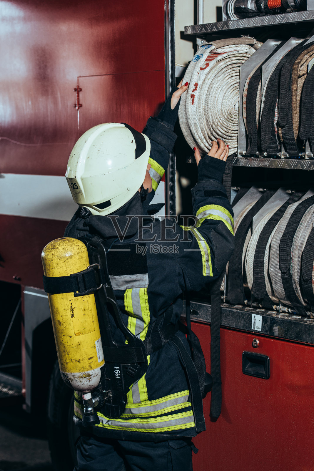 部分视图的女性消防队员与灭火器的背面把水带到消防车在消防部门照片摄影图片