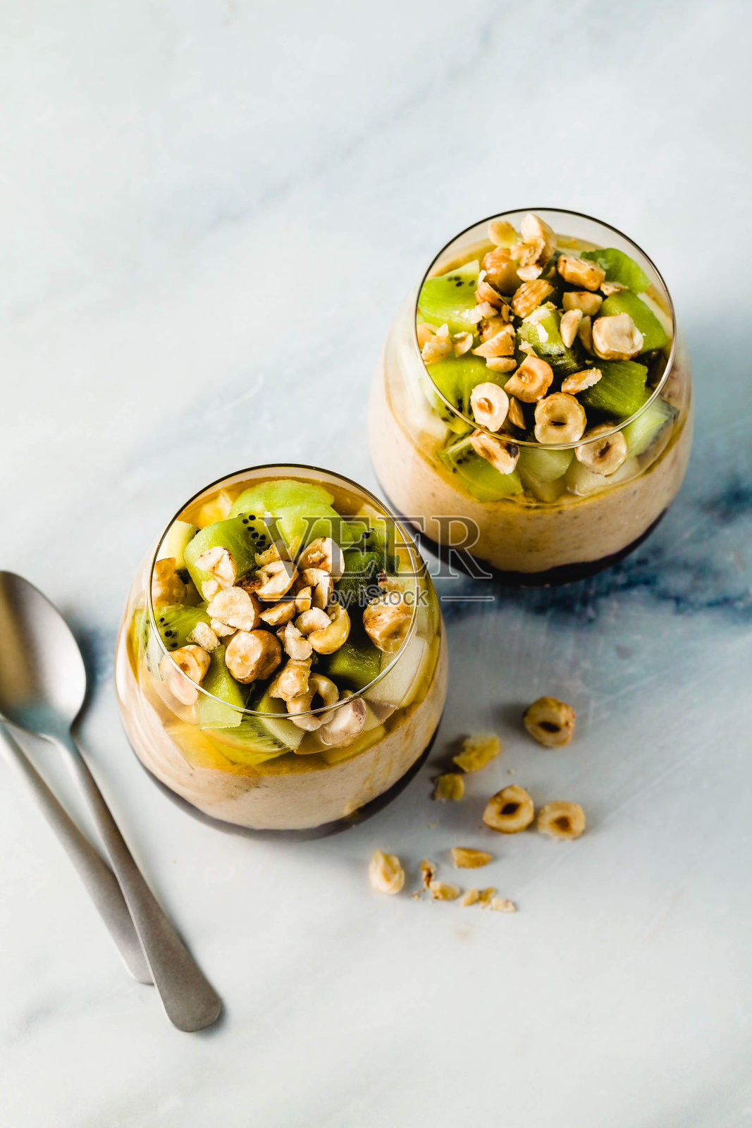 素食香蕉分层甜点绿荞麦，奇亚籽和藜麦与蓝莓果酱在一个玻璃杯与新鲜水果，坚果和蜂蜜。健康的早餐。照片摄影图片