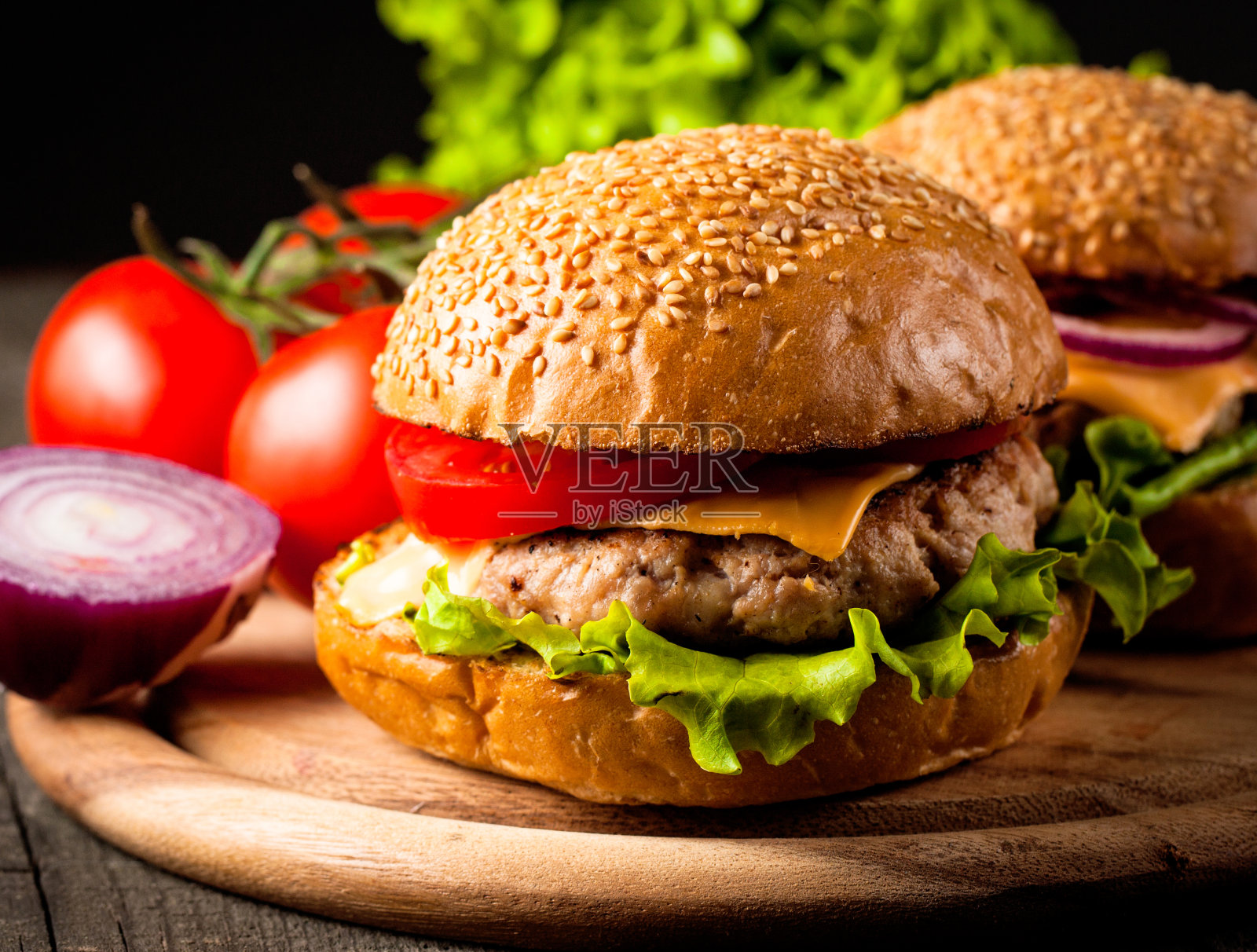 自制汉堡的特写照片，啤酒由牛肉、洋葱、番茄、生菜、奶酪和香料制成。新鲜的汉堡特写在木制的乡村桌子和土豆薯条和薯条。照片摄影图片