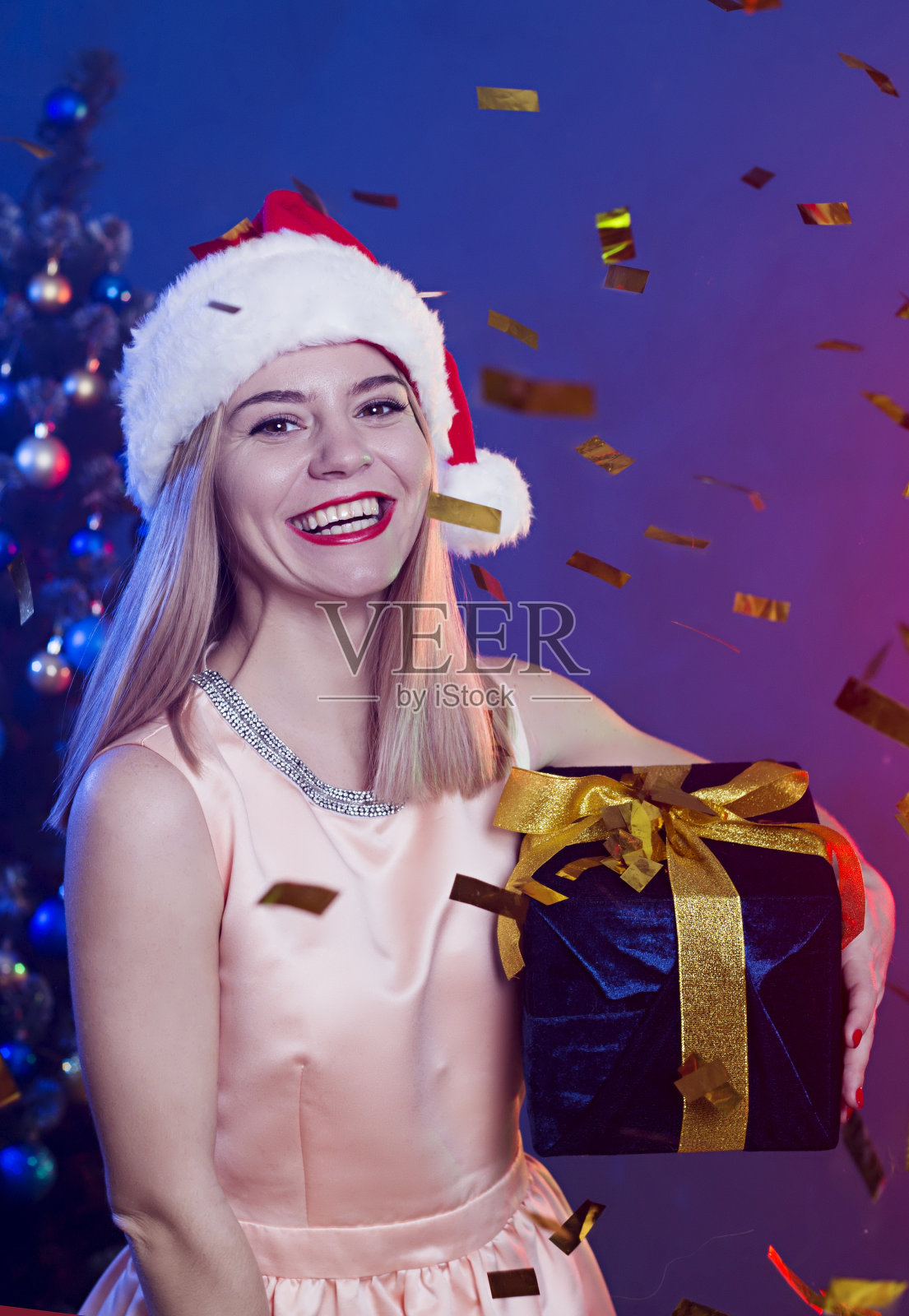 幸福美丽的年轻微笑金发女人在圣诞老人帽子和大礼盒在手里照片摄影图片