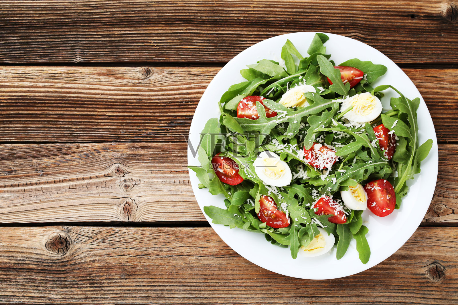 棕色的木桌上放着芝麻菜叶、西红柿和鸡蛋的沙拉照片摄影图片