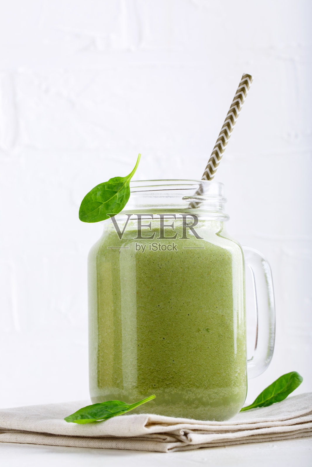 绿色冰沙饮料在玻璃罐上白色。混合了菠菜和绿荞麦的鸡尾酒。健康的素食。照片摄影图片