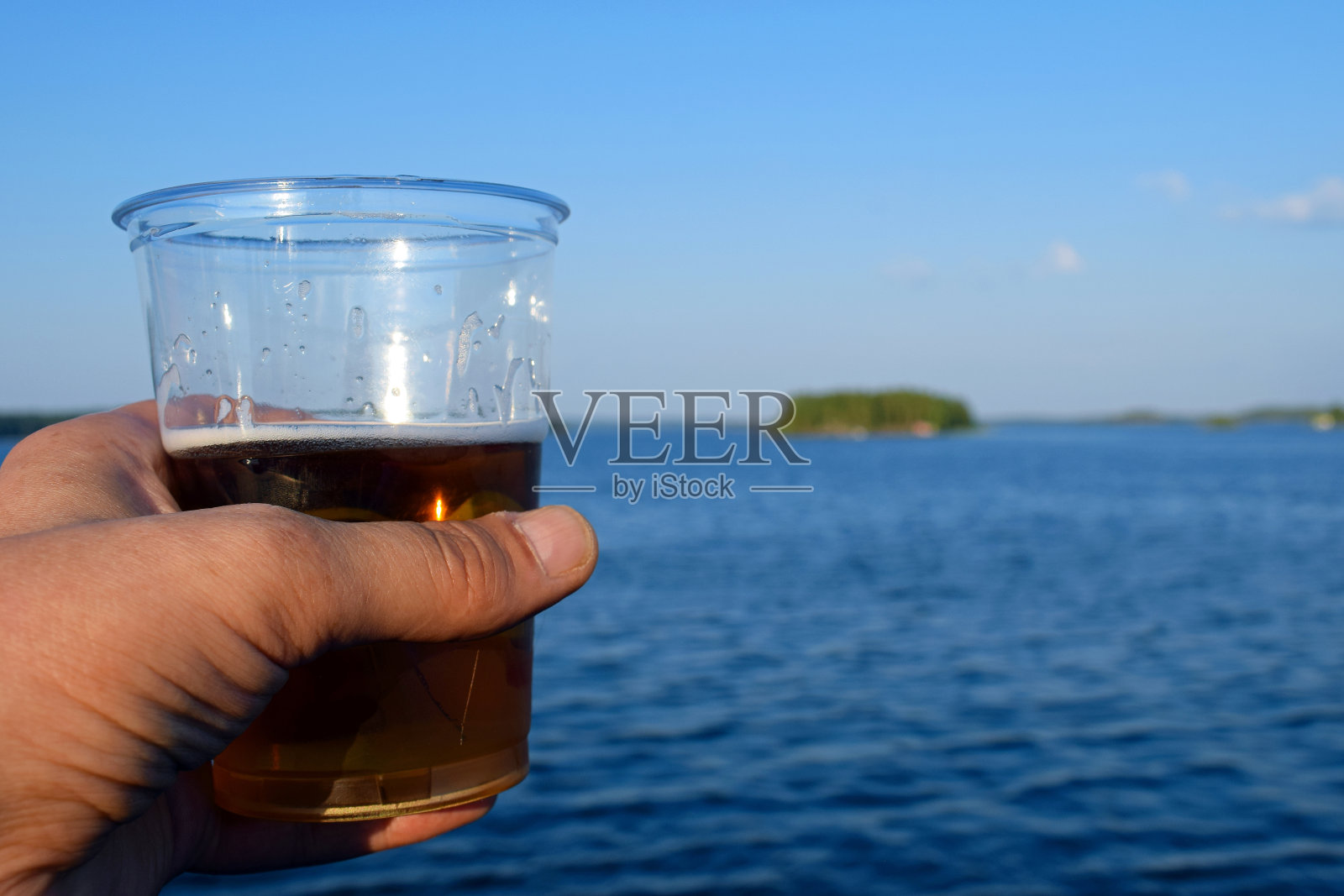 在夏日手里拿着啤酒。美丽的湖泊景观的背景。照片摄影图片