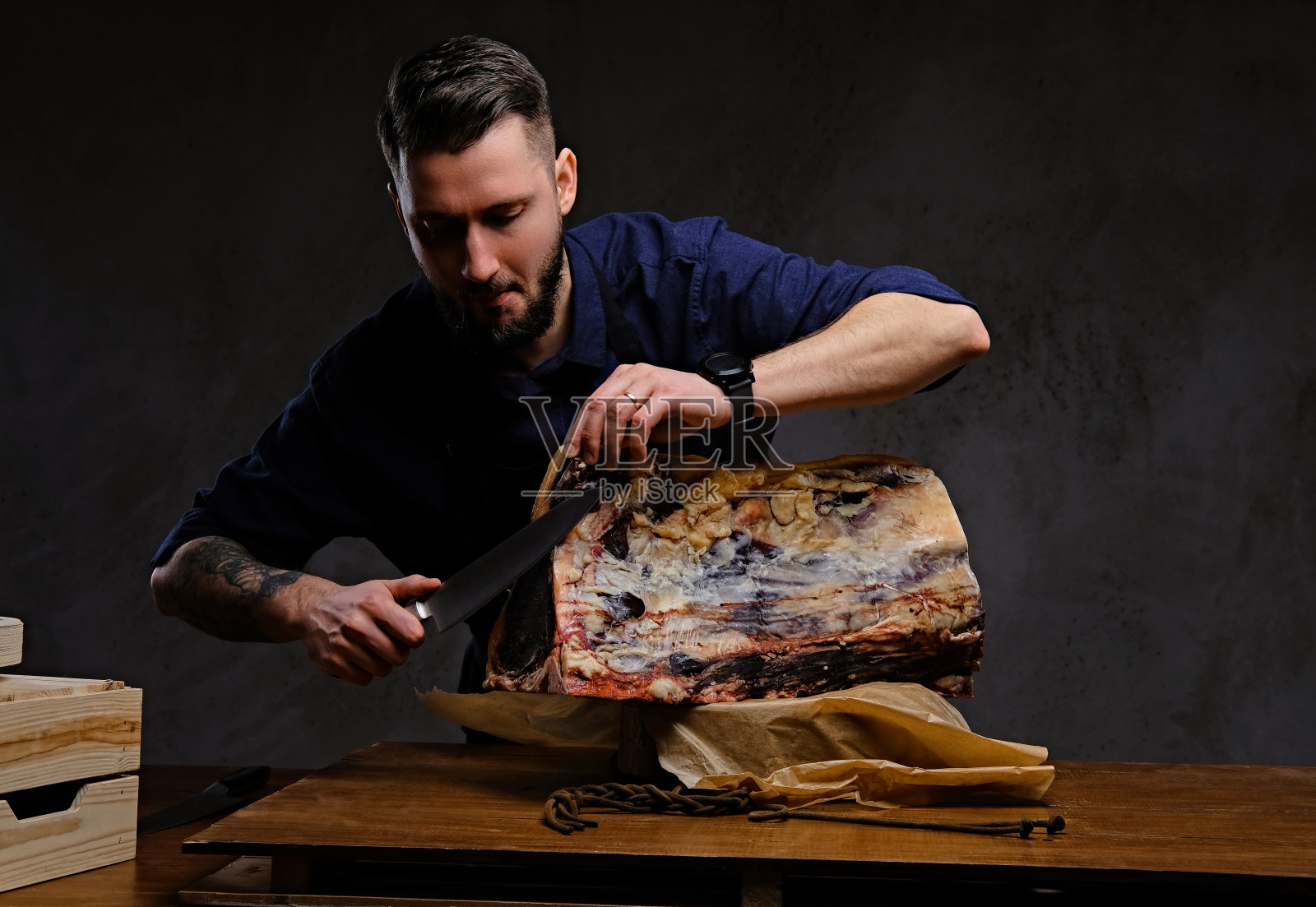 专注厨师厨师切独家肉干在一个狩猎房子的桌子上在黑暗的背景。照片摄影图片