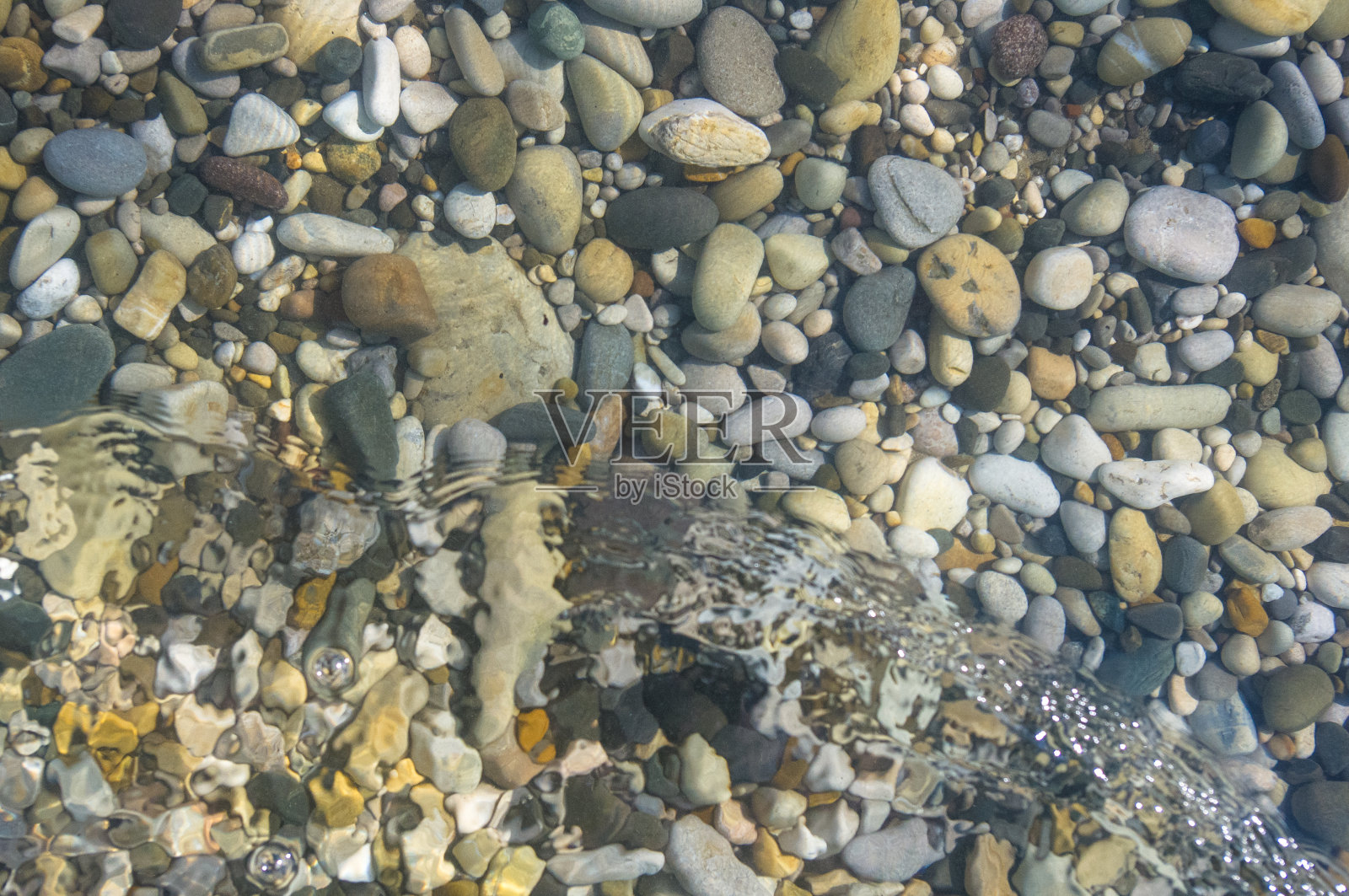 海卵石滩上有五颜六色的石头，浪花上有泡沫照片摄影图片