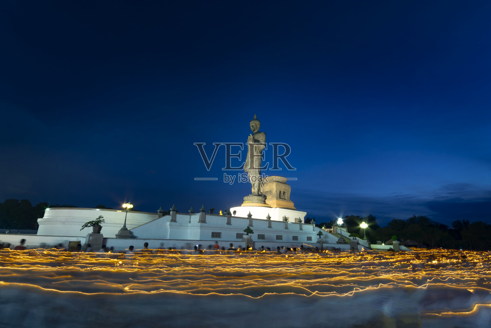 许多泰国人举着蜡烛绕着佛像走。照片摄影图片