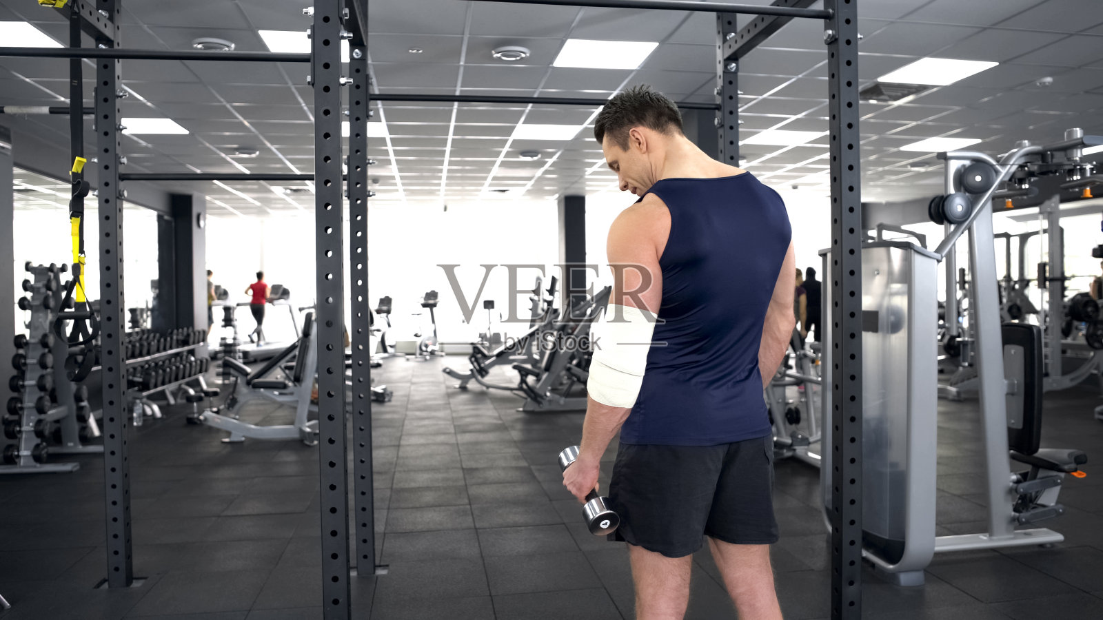 肌肉发达的男子肘部受伤，在运动俱乐部用哑铃训练，恢复照片摄影图片