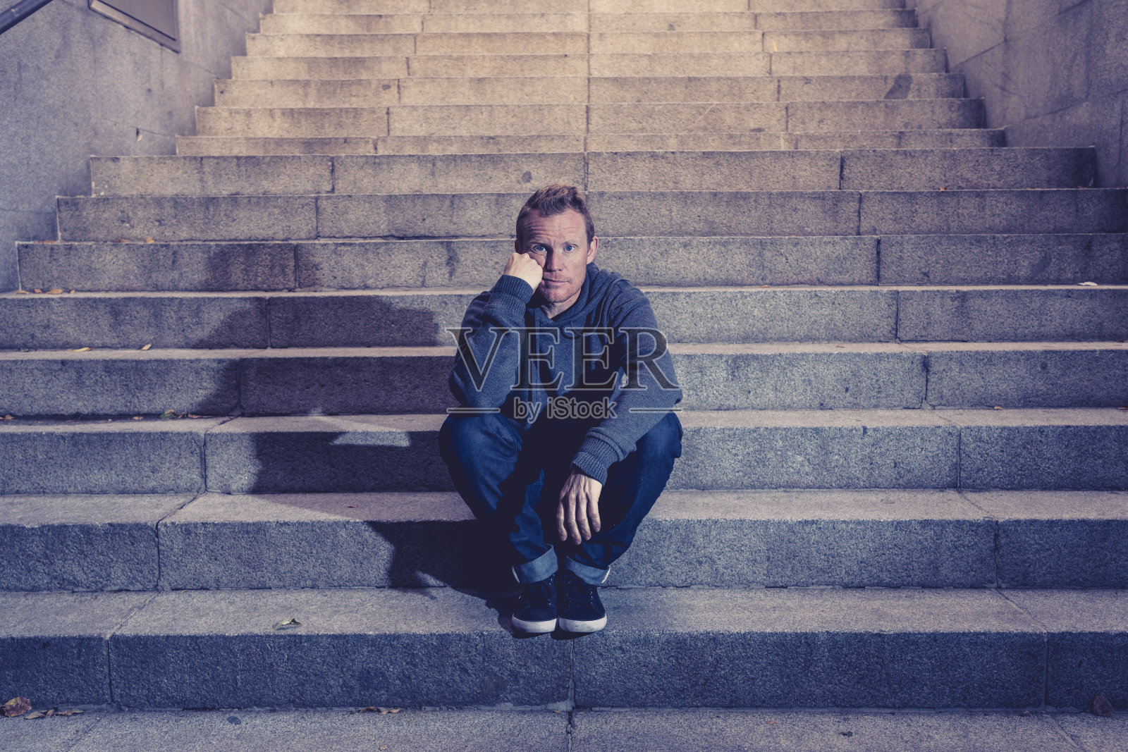 年轻的失业商人遭受抑郁症坐在地面街道地下独自靠在墙上看起来绝望的情感痛苦心理健康失业和人类情感的概念。照片摄影图片