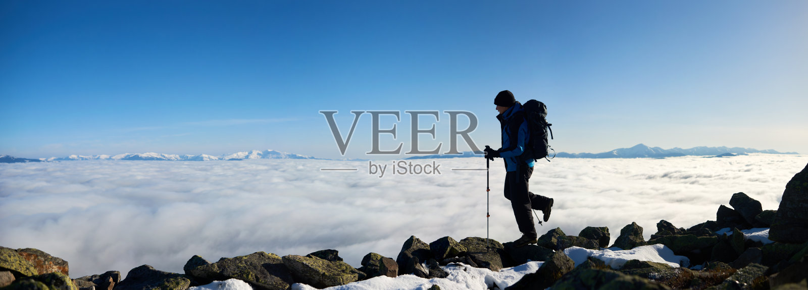 徒步旅行者在岩石山在雾谷与白云，雪山和蓝天的背景。照片摄影图片