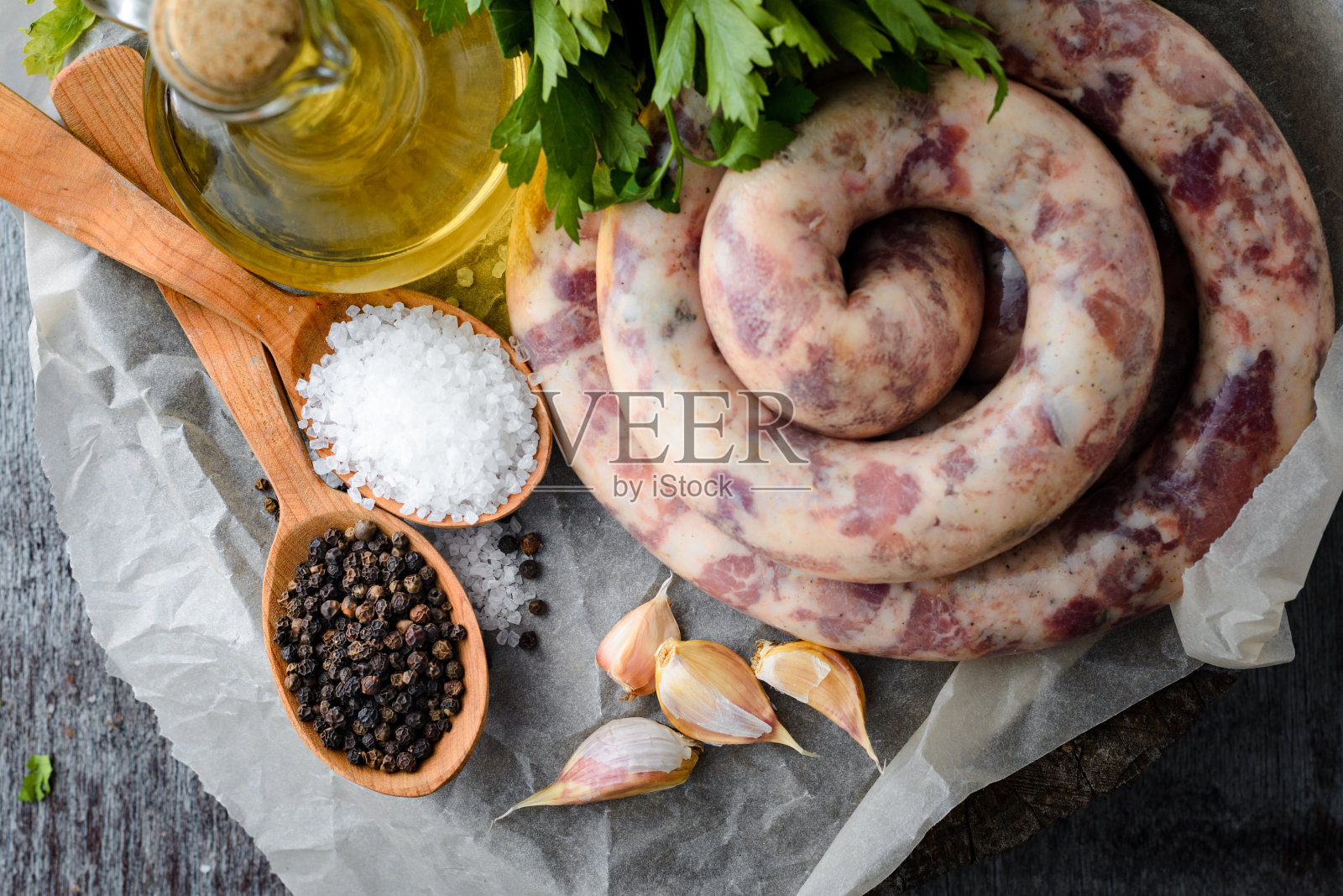 自制香肠、香料、大蒜、橄榄油和欧芹放在一张木桌上。照片摄影图片