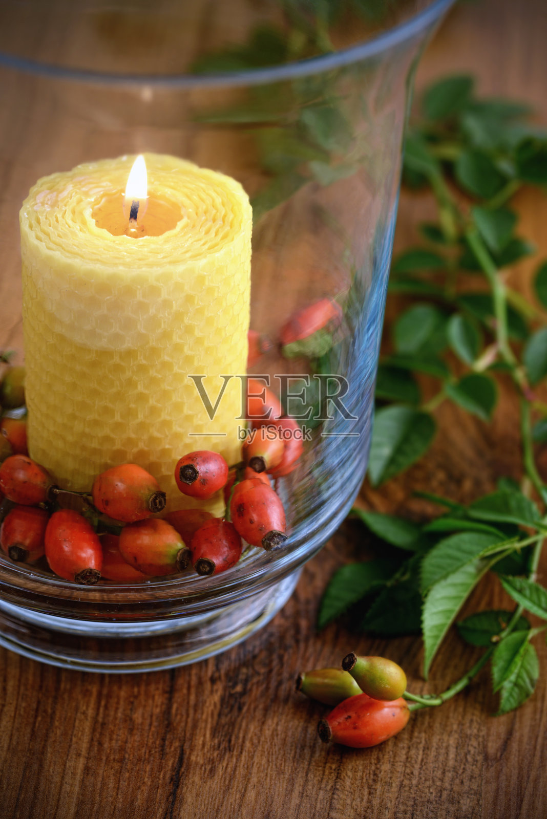 玻璃蜂蜡蜡烛与玫瑰果。秋天的装饰。照片摄影图片