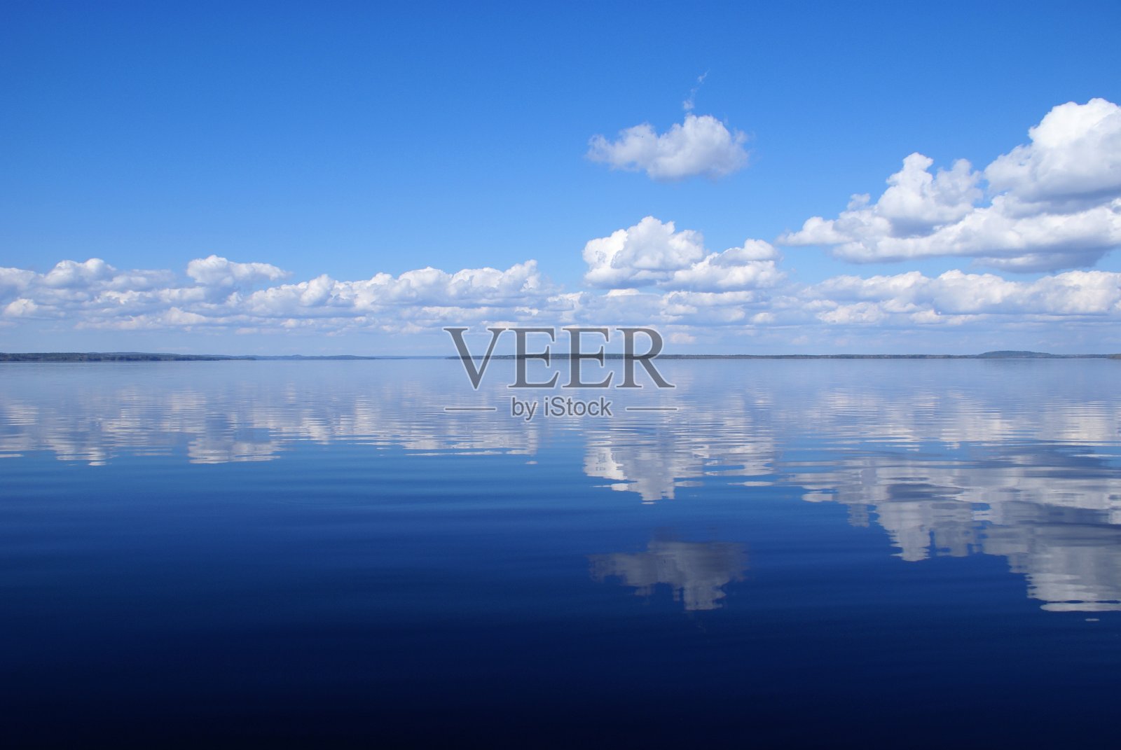 美丽平静的蓝色湖泊与白云在水中的反射。天气晴朗，阳光灿烂。天空是蓝色的。地平线上的岛屿。照片摄影图片
