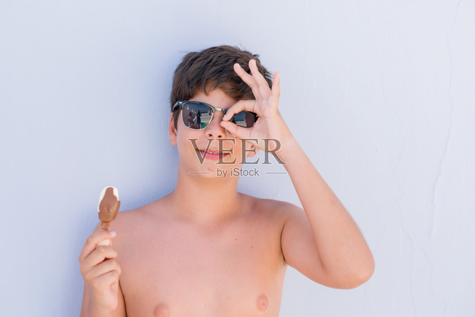 孩子在节日吃冰淇淋，快乐的脸，微笑，做ok手势，手，眼睛透过手指看照片摄影图片