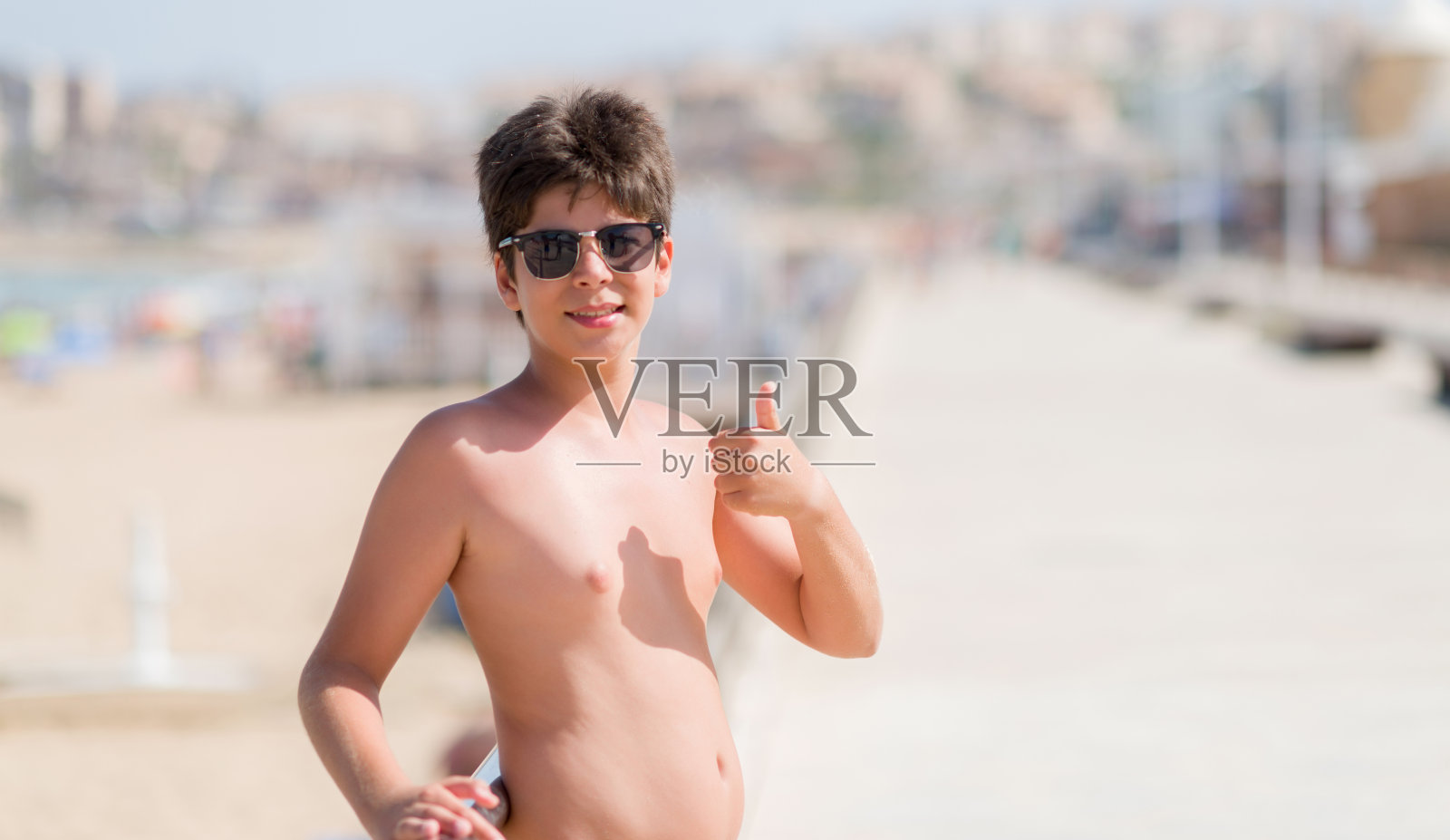 小孩子在假期的海滩上开心地笑着做ok手势，用手指竖起大拇指，很棒的手势照片摄影图片