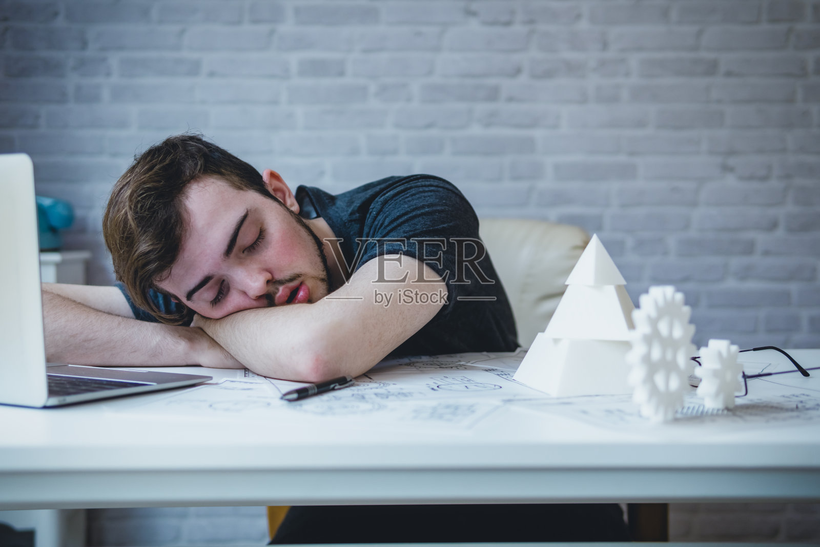 工程人员工作过度，睡在桌子上的蓝图机械零件在办公室。有不良的压力和过度工作的观念照片摄影图片