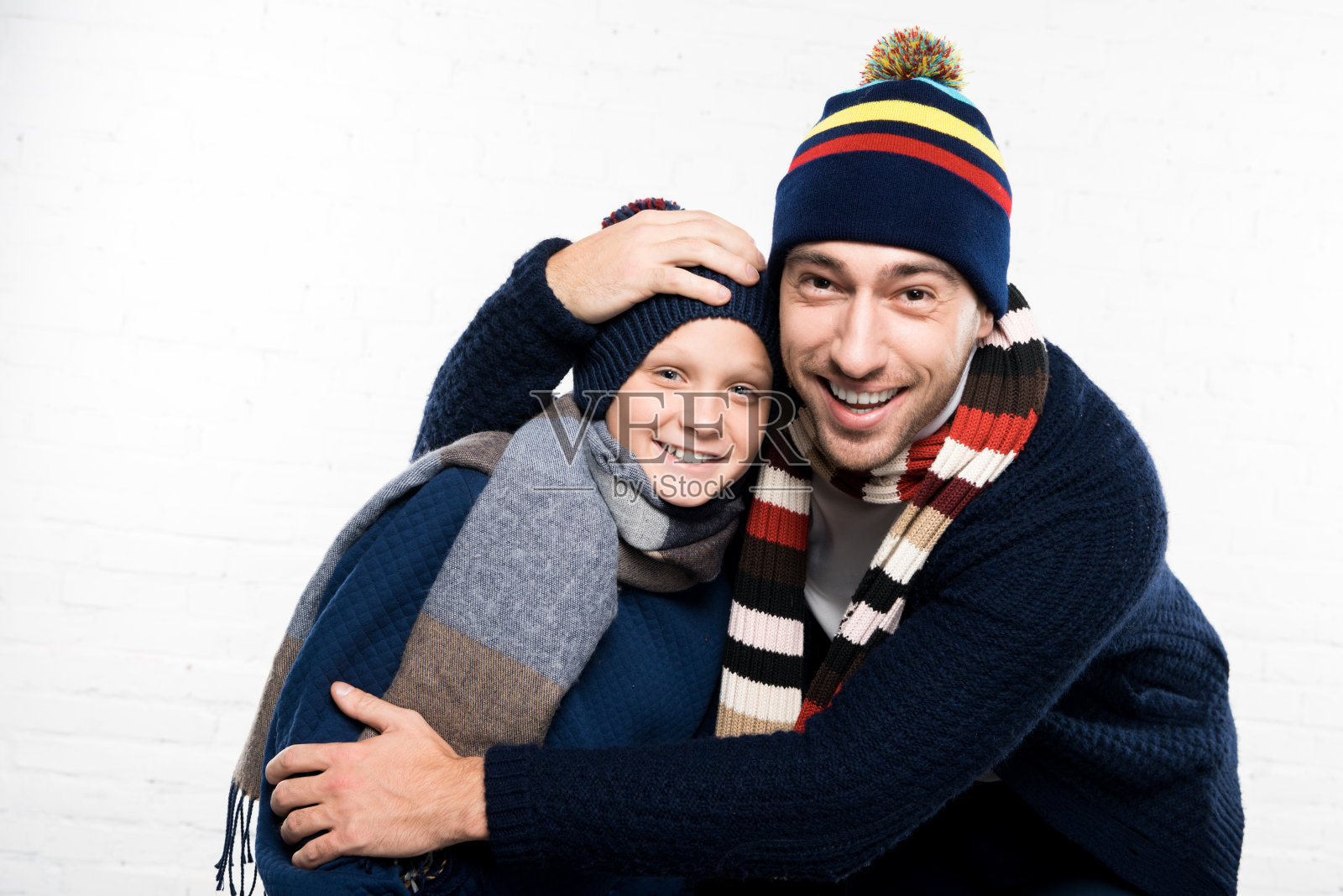 微笑的父亲和儿子穿着冬装在白色的背景看着相机照片摄影图片