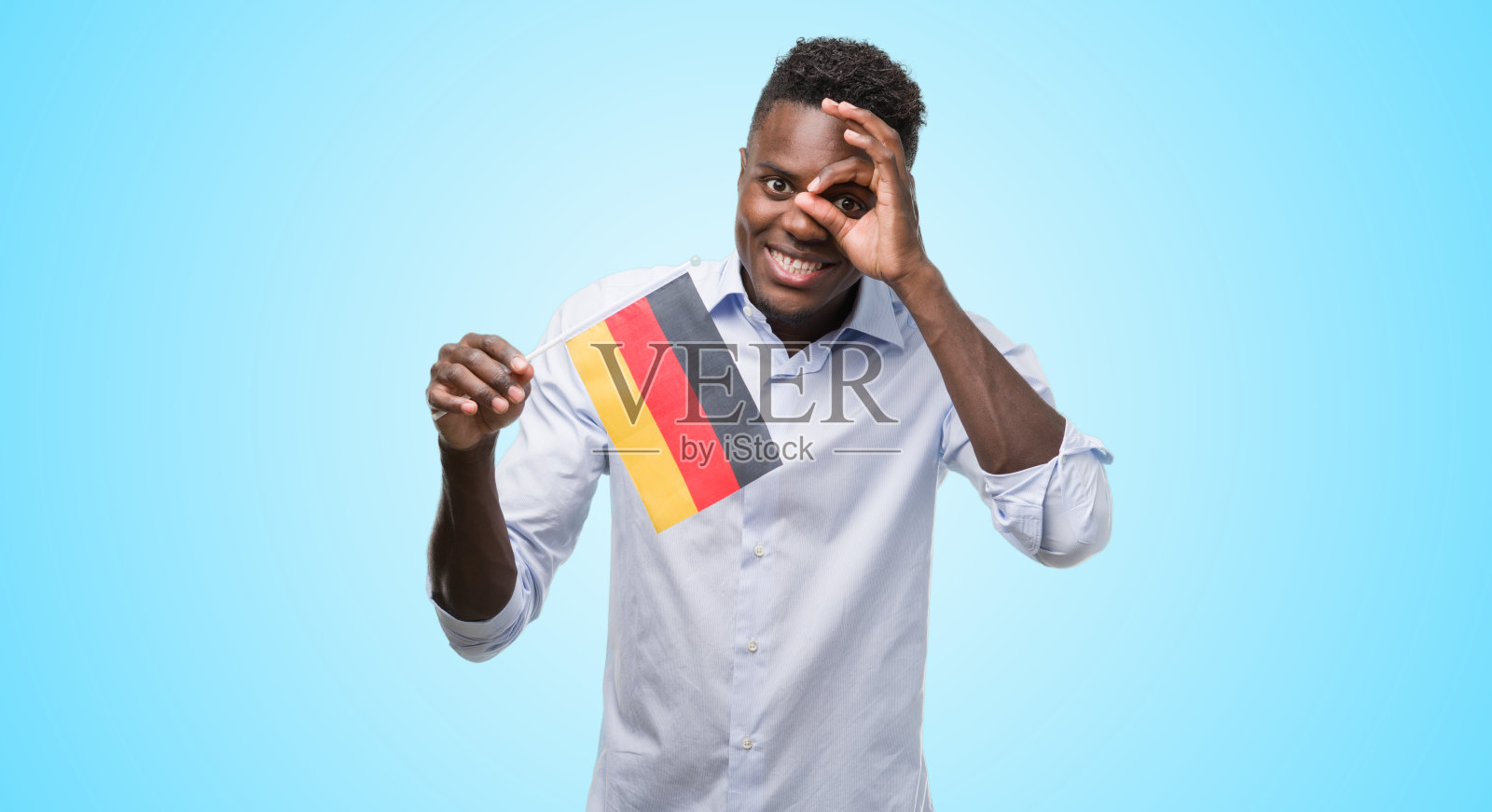 年轻的非洲裔美国人举着德国国旗与快乐的脸微笑做ok手势与手在眼睛透过手指看照片摄影图片