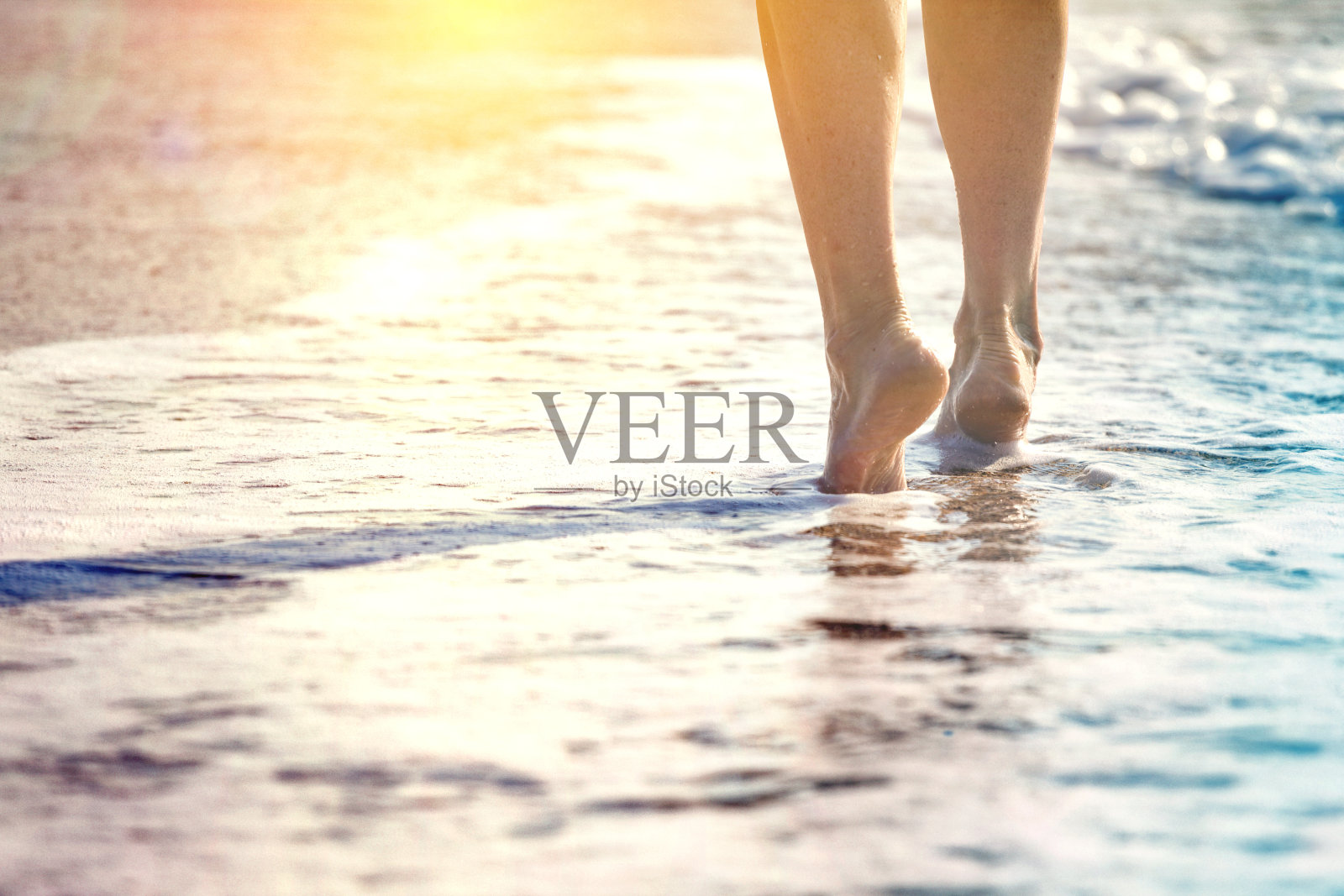 在夏天的海滩上，年轻女子沿着海浪的海水和沙子走着。旅行概念。n照片摄影图片