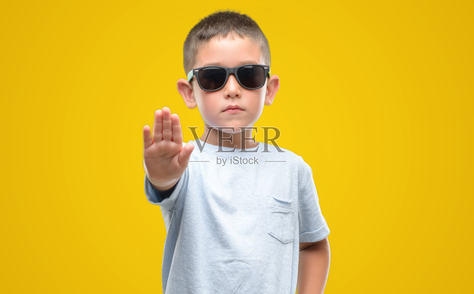 黑头发小孩戴着墨镜，摊开双手做着停止手势，表情严肃自信，做着防卫姿势照片摄影图片