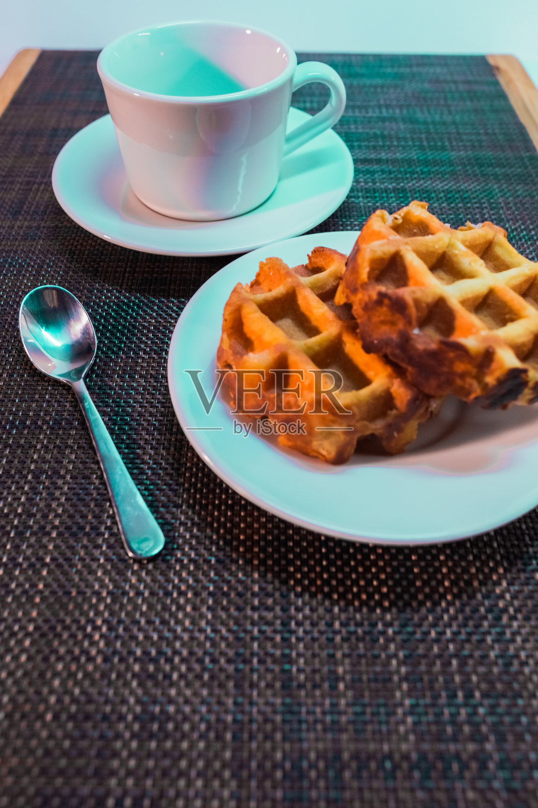 白色的杯子放在碟子上，勺子和圆形的维也纳华夫饼放在白色的碟子上照片摄影图片