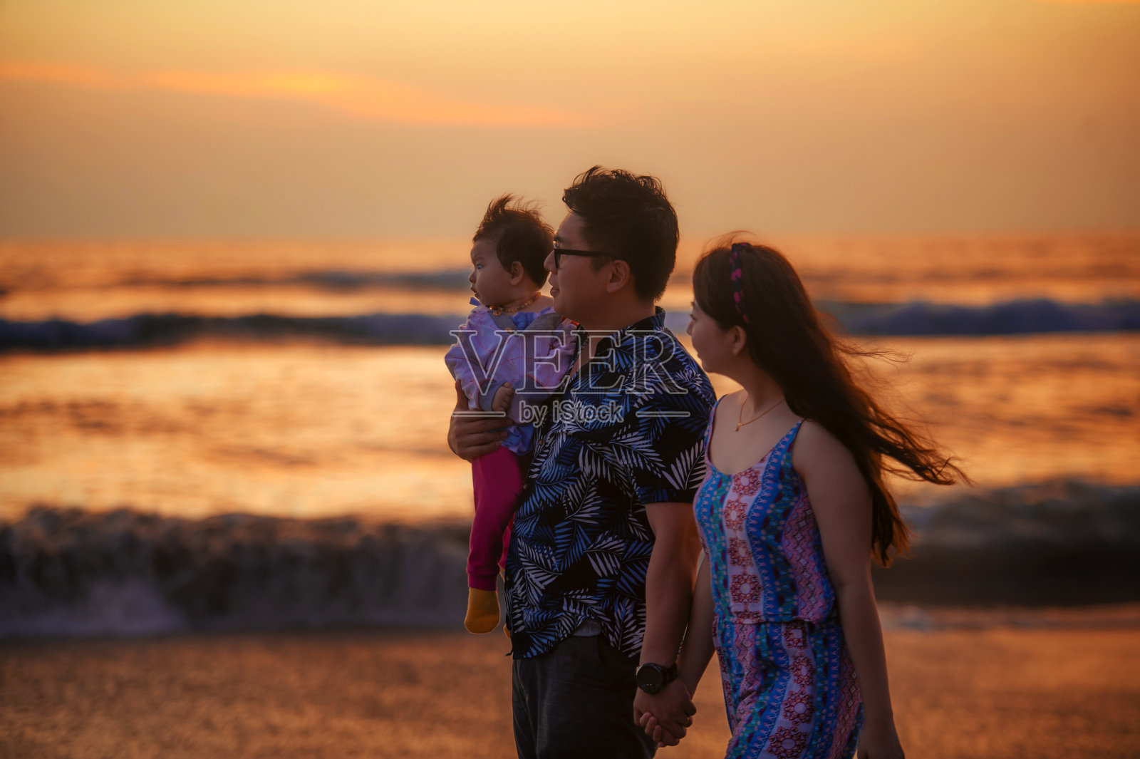 年轻幸福和美丽的亚洲华人夫妇抱着宝贝女儿走在日落海滩上享受一起浪漫的暑假旅行在家庭甜蜜的假期概念照片摄影图片