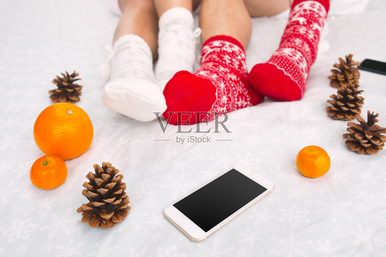 软照片的女人和男人在床上与手机和水果，顶部的观点。女性和男性的腿在温暖的羊毛袜子照片摄影图片