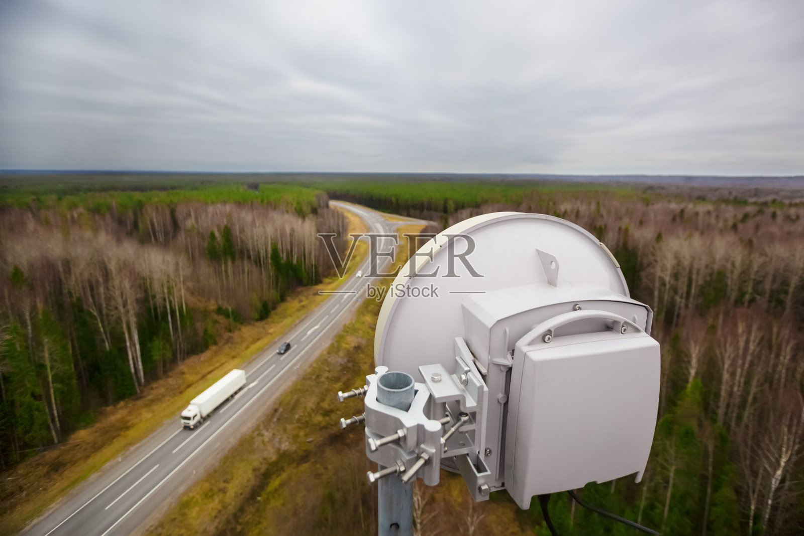 阴天环境下的户外高容量微波通信塔架和带天线的载波级分组设备。以汽车为背景的森林和高速公路。照片摄影图片