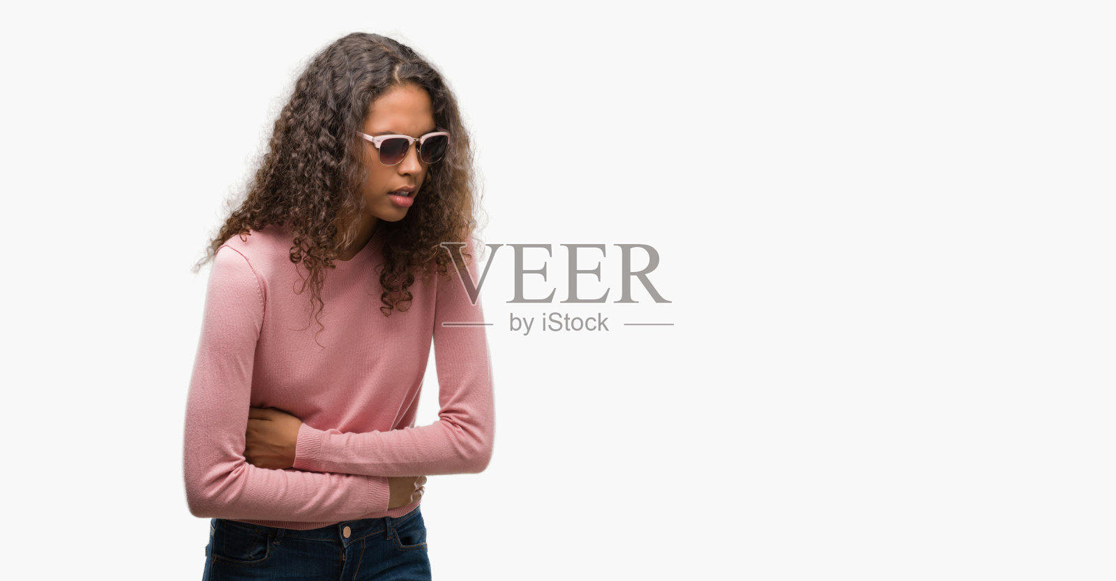 年轻漂亮的西班牙女子戴着墨镜，手放在肚子上，因为恶心，痛苦的疾病感觉不舒服。疼痛的概念。照片摄影图片