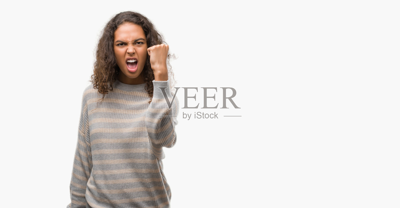 美丽的年轻西班牙妇女穿着条纹毛衣愤怒和疯狂举起拳头沮丧和愤怒，而大喊与愤怒。愤怒和侵略性的概念。照片摄影图片