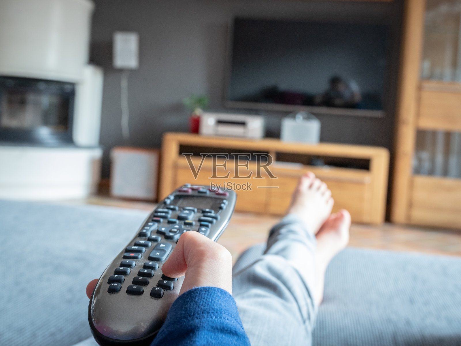 孩子的手按着现代遥控器，并指在电视机上。脚在沙发上照片摄影图片