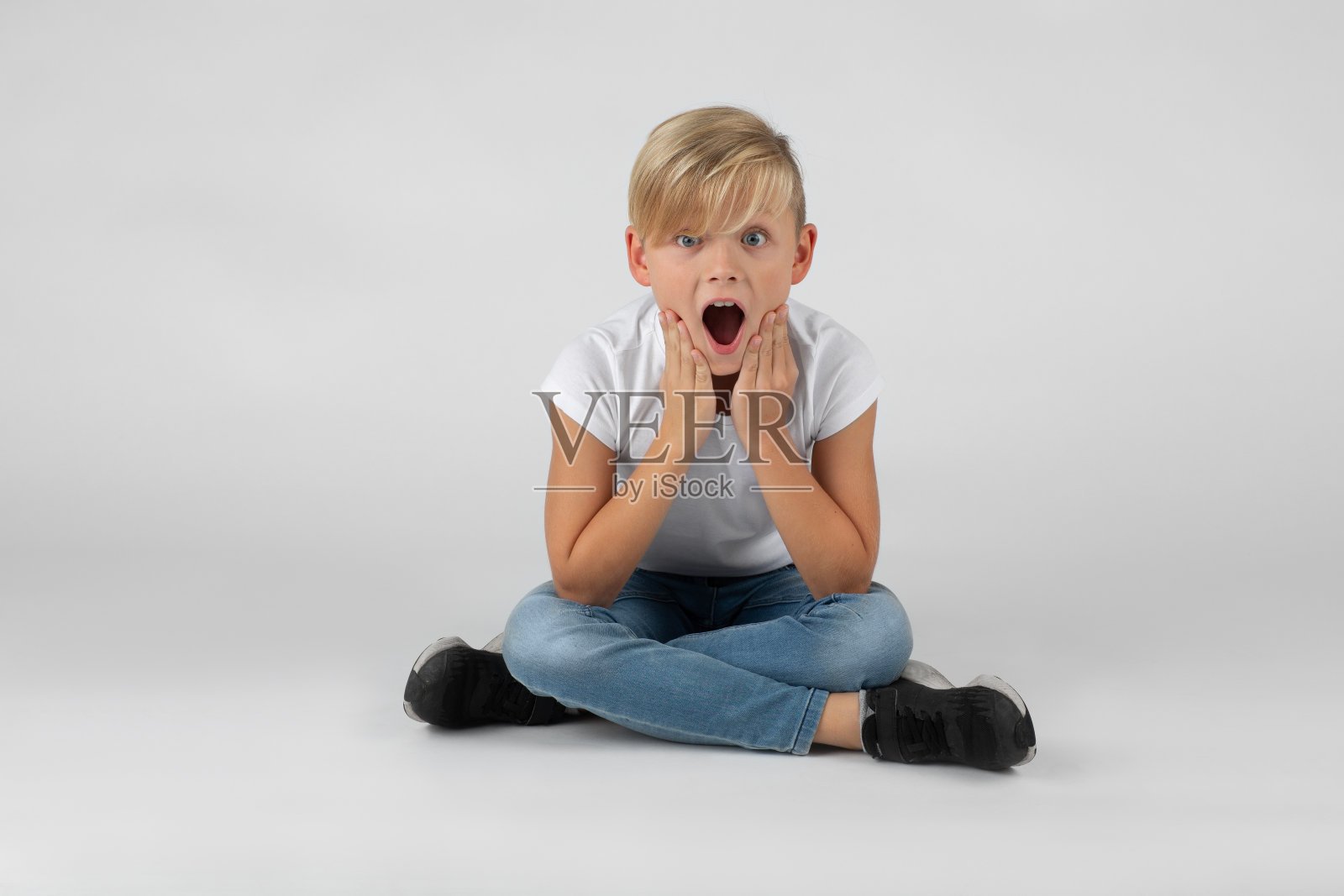 金发小男孩坐在地板上，很惊讶照片摄影图片