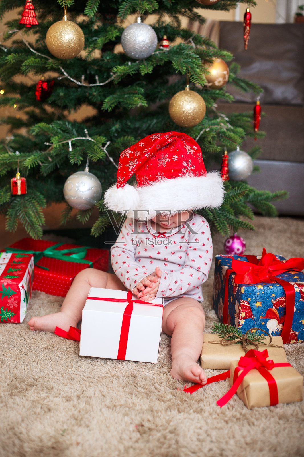 快乐可爱的小女孩戴着圣诞老人的帽子在圣诞树下拿着圣诞礼物在家照片摄影图片