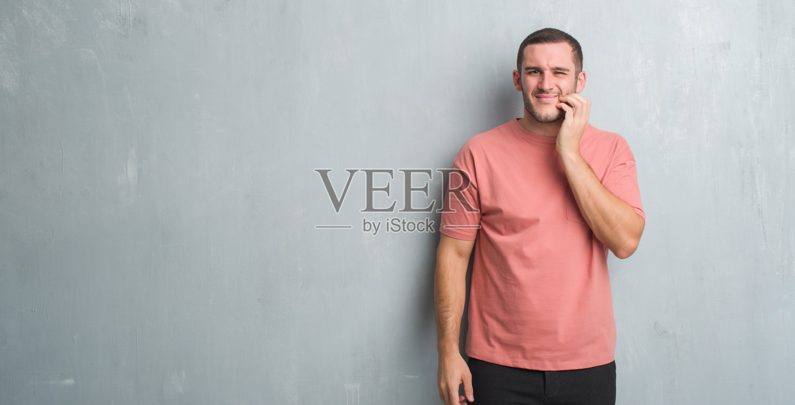 年轻的白种人越过灰色垃圾墙触摸嘴与手痛苦的表情因为牙痛或牙齿疾病的牙齿。牙医的概念。照片摄影图片