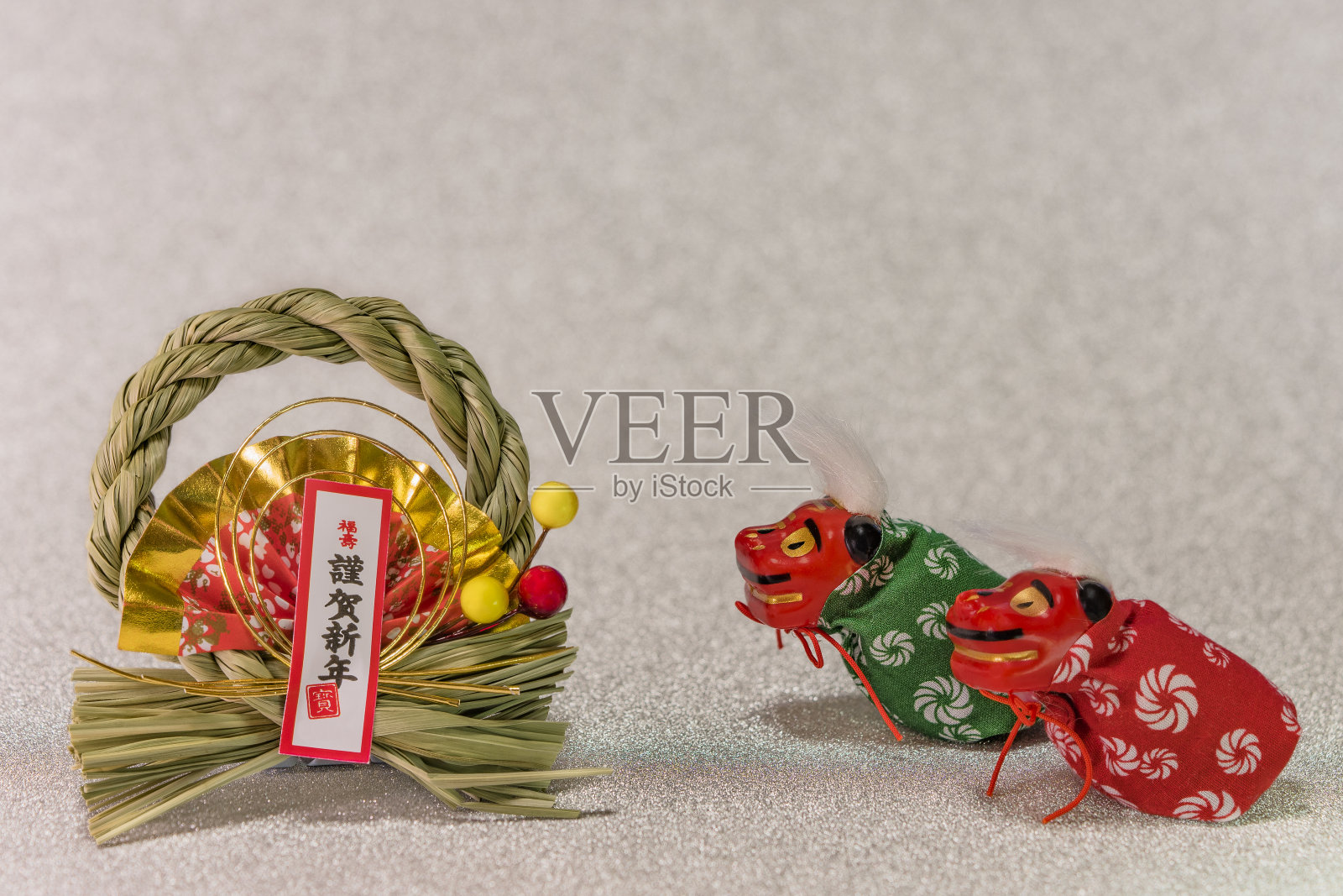 日本新年贺卡的表意文字gingashinen，意思是新年快乐的可爱的日本民间动物雕像的两只狮子石mai，折纸制作的范围和稻草装饰与松果在闪闪发光的银背景。照片摄影图片