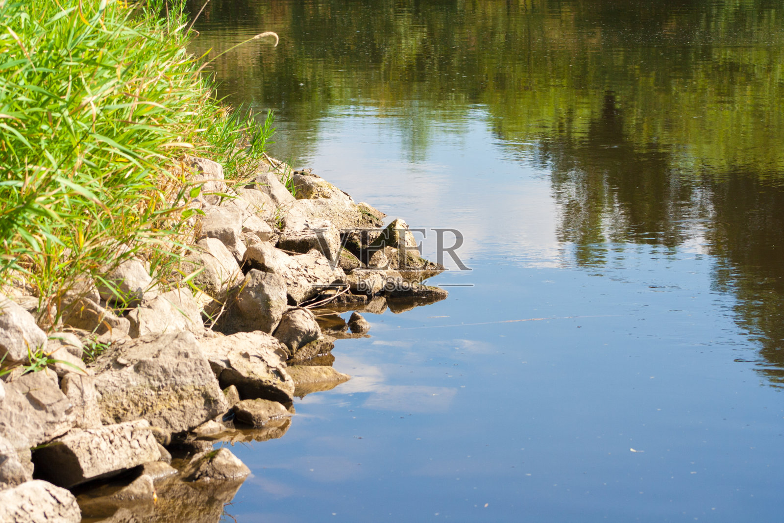 美丽的河景。河水倒映着天空和岸边的植物。岸边铺满了石头。照片摄影图片