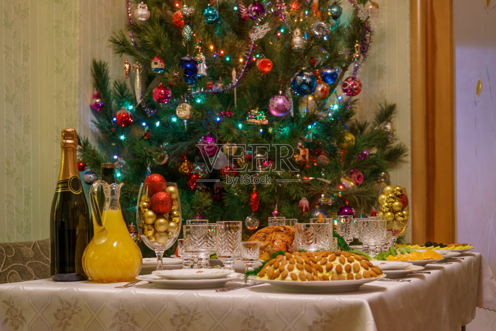 餐桌上的节日菜肴靠近美丽装饰的圣诞树在客厅内部。新年假期在舒适的家的概念。的语气照片摄影图片