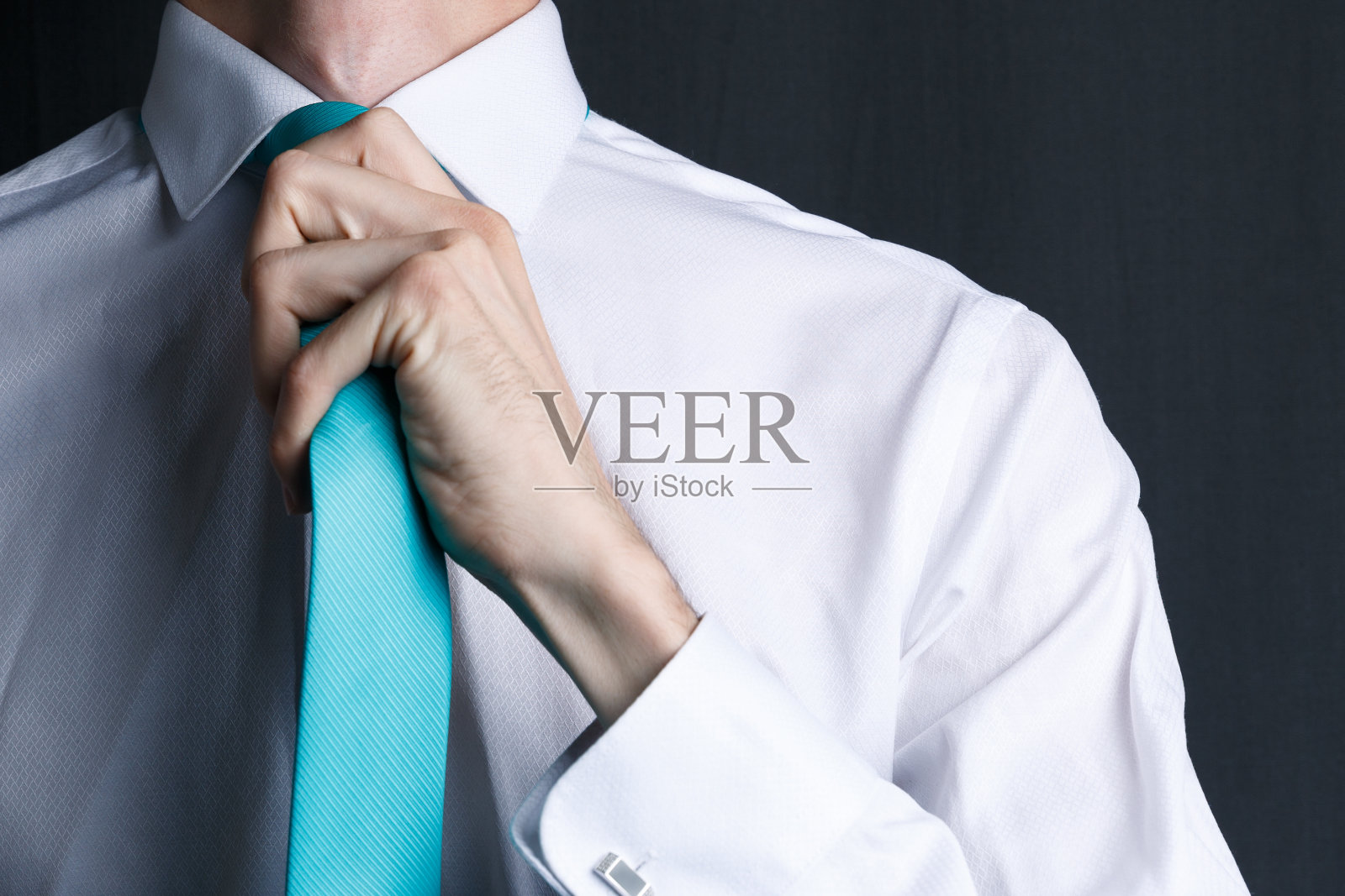 特写年轻男子在白色衬衫与领带。那人正了正领带，脸上没有刮胡子。穿着白衬衫，打着绿松石领带的商人。黑暗的背景。本空间照片摄影图片