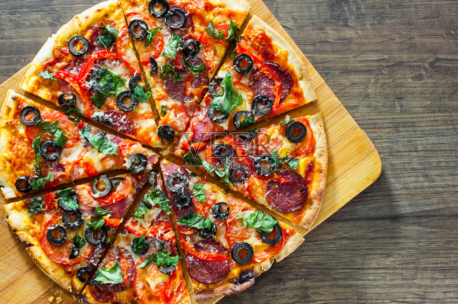 披萨切片配马苏里拉芝士，意大利腊肠，胡椒，意大利辣香肠，西红柿，橄榄，香料和新鲜罗勒。木质背景的意大利披萨照片摄影图片