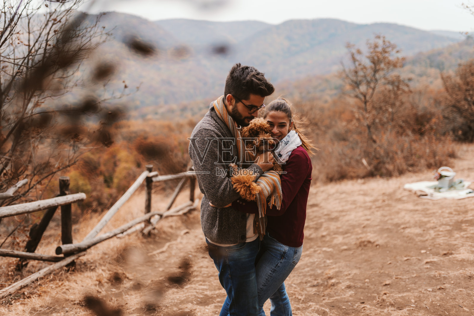 一对情侣在大自然中拥抱他们的宠物。穿上暖和的衣服，秋高气爽。背景是森林和山脉。照片摄影图片