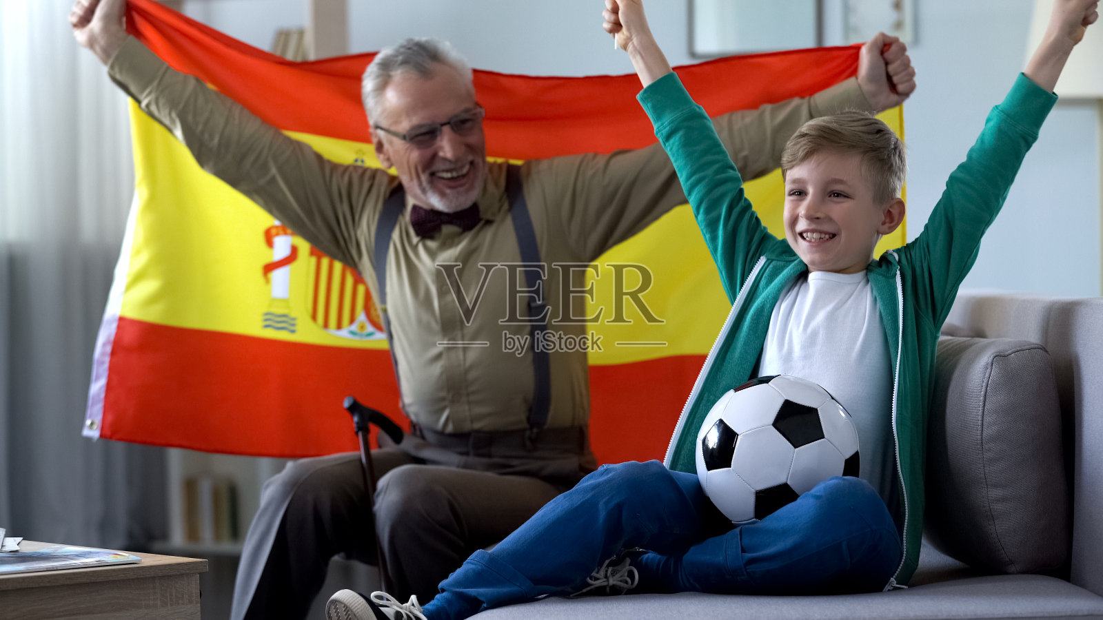 爷爷挥舞着西班牙国旗，和男孩一起庆祝足球队的胜利照片摄影图片